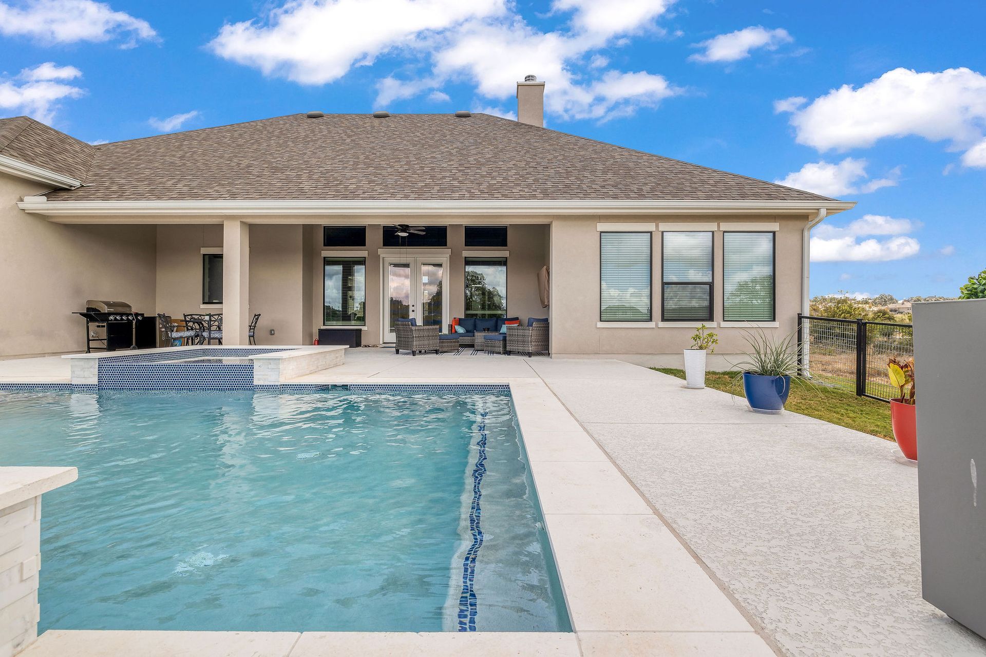 Backyard pool beside a beige house with a covered patio and desert landscaping