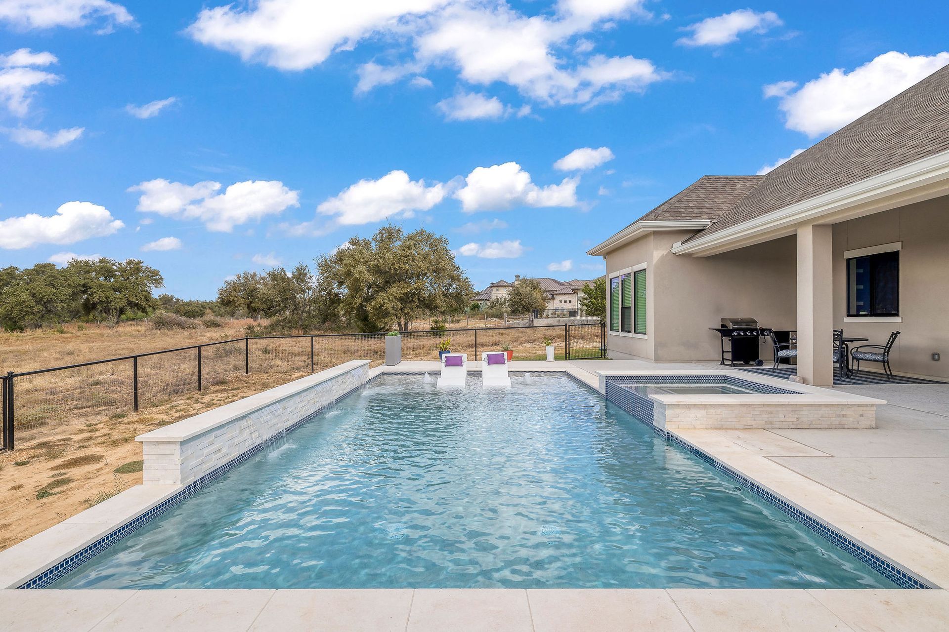 Backyard pool beside a beige house with a covered patio and desert landscaping