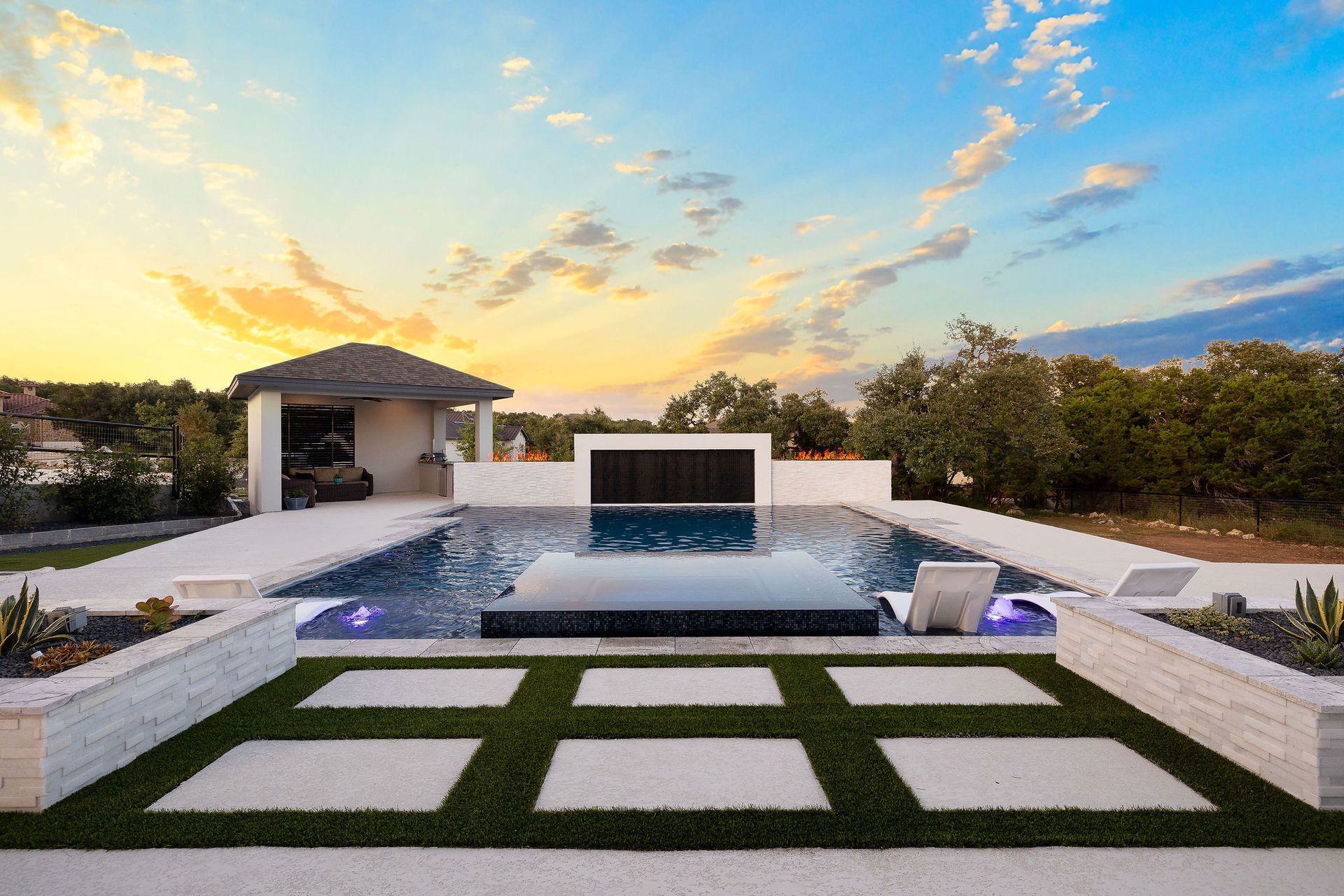 Modern backyard with pool, fire feature, and manicured lawn at sunset
