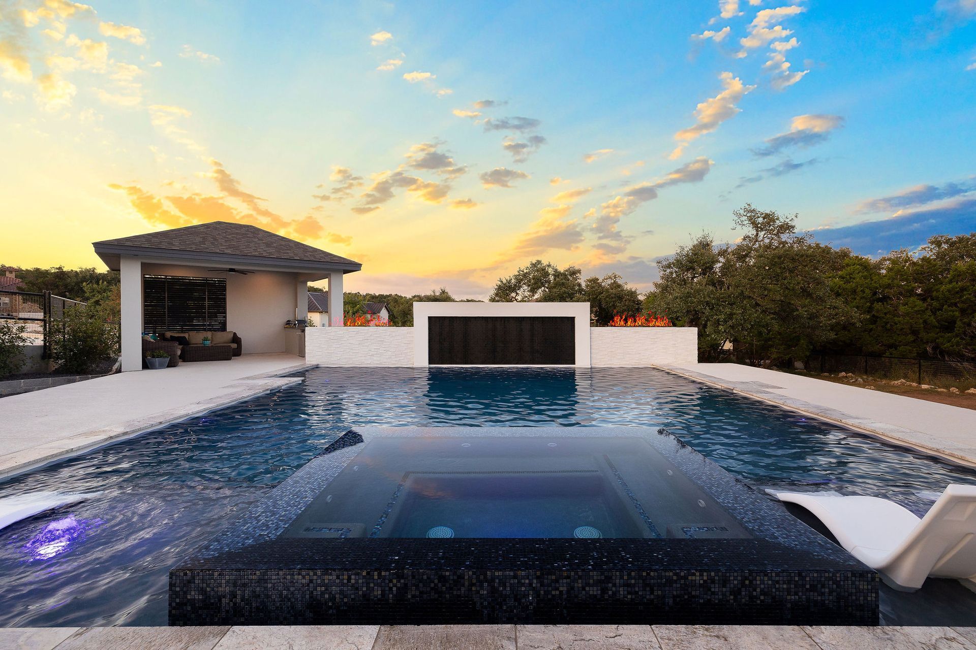 Modern infinity pool at sunset with a distant ocean view and a small cabana.