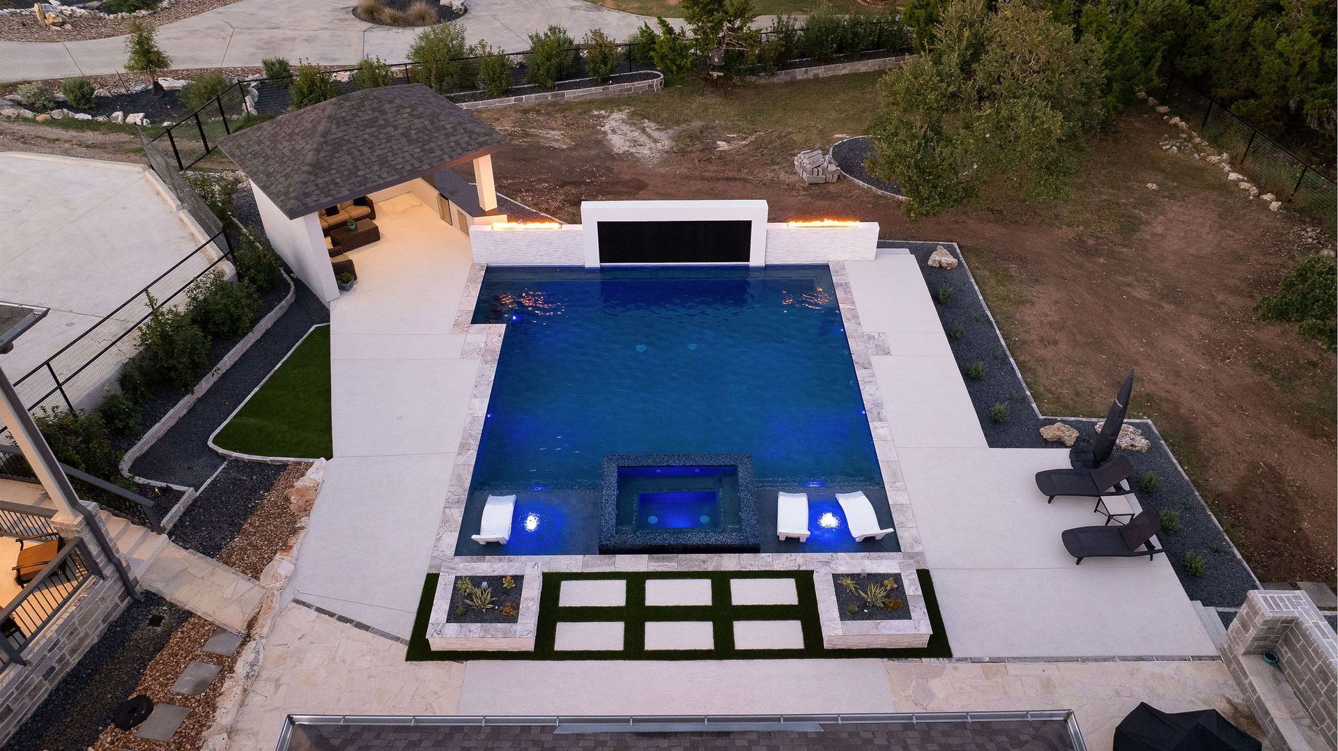 Modern poolside patio at night with a fire wall, lit house, and starry sky