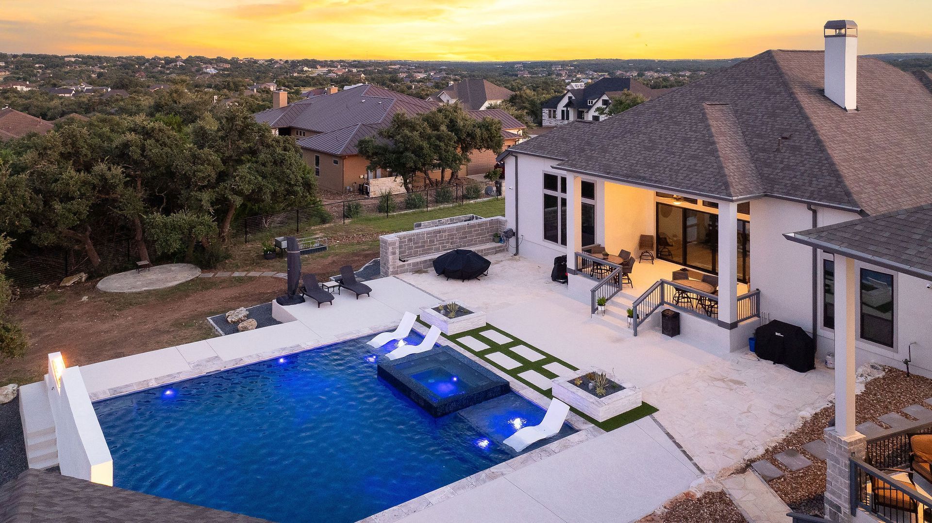 Modern poolside patio at night with a fire wall, lit house, and starry sky