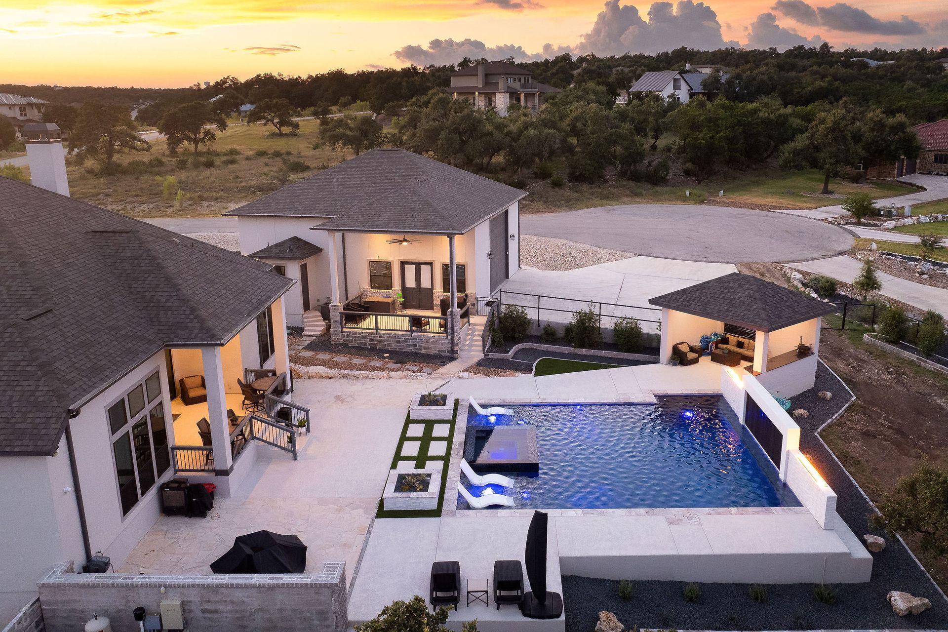 Luxury villa courtyard with lit swimming pool at sunset and surrounding white buildings