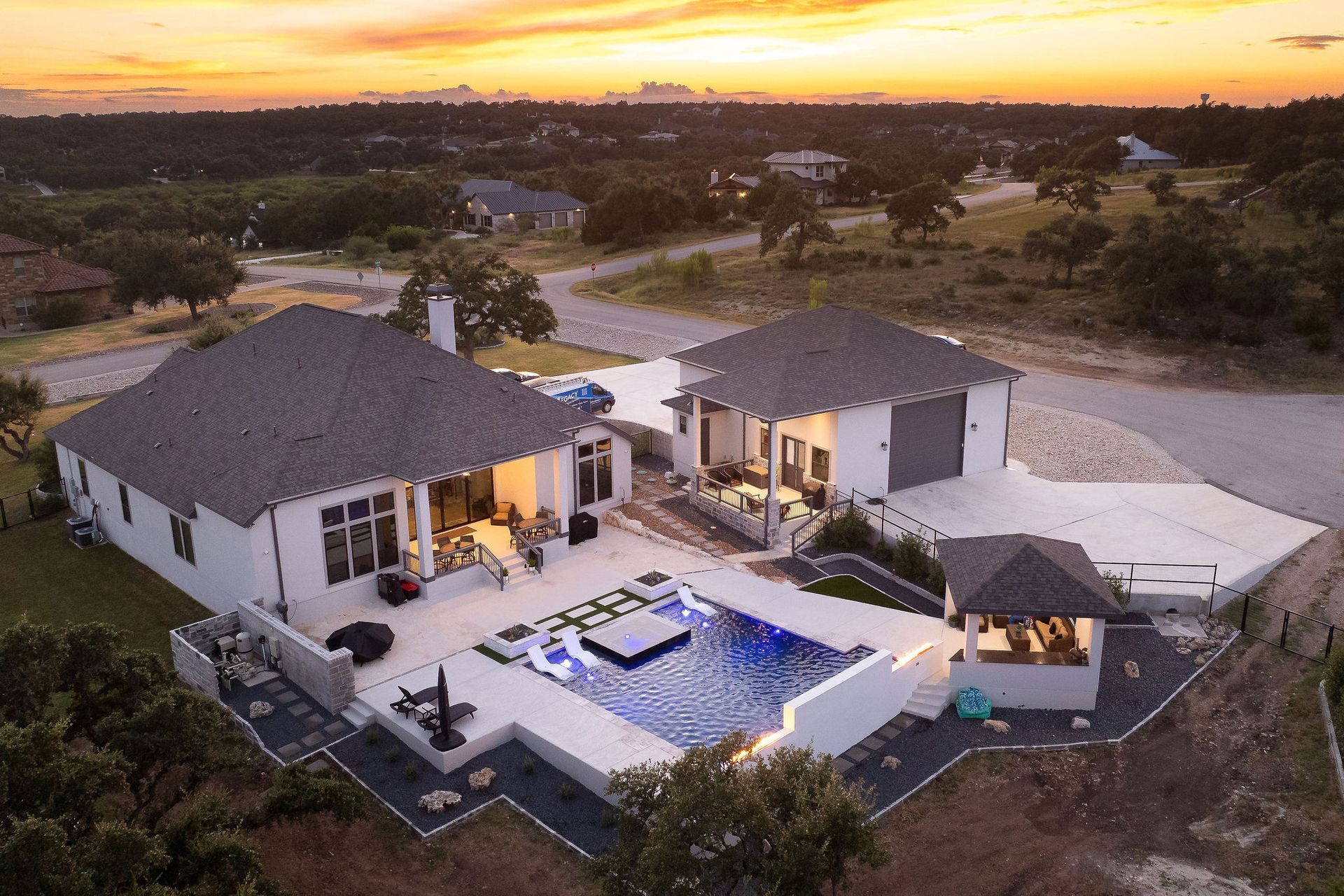 Luxury villa courtyard with lit swimming pool at sunset and surrounding white buildings