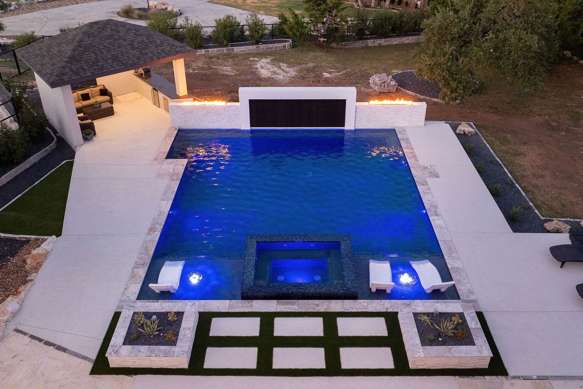 Luxury villa courtyard with lit swimming pool at sunset and surrounding white buildings