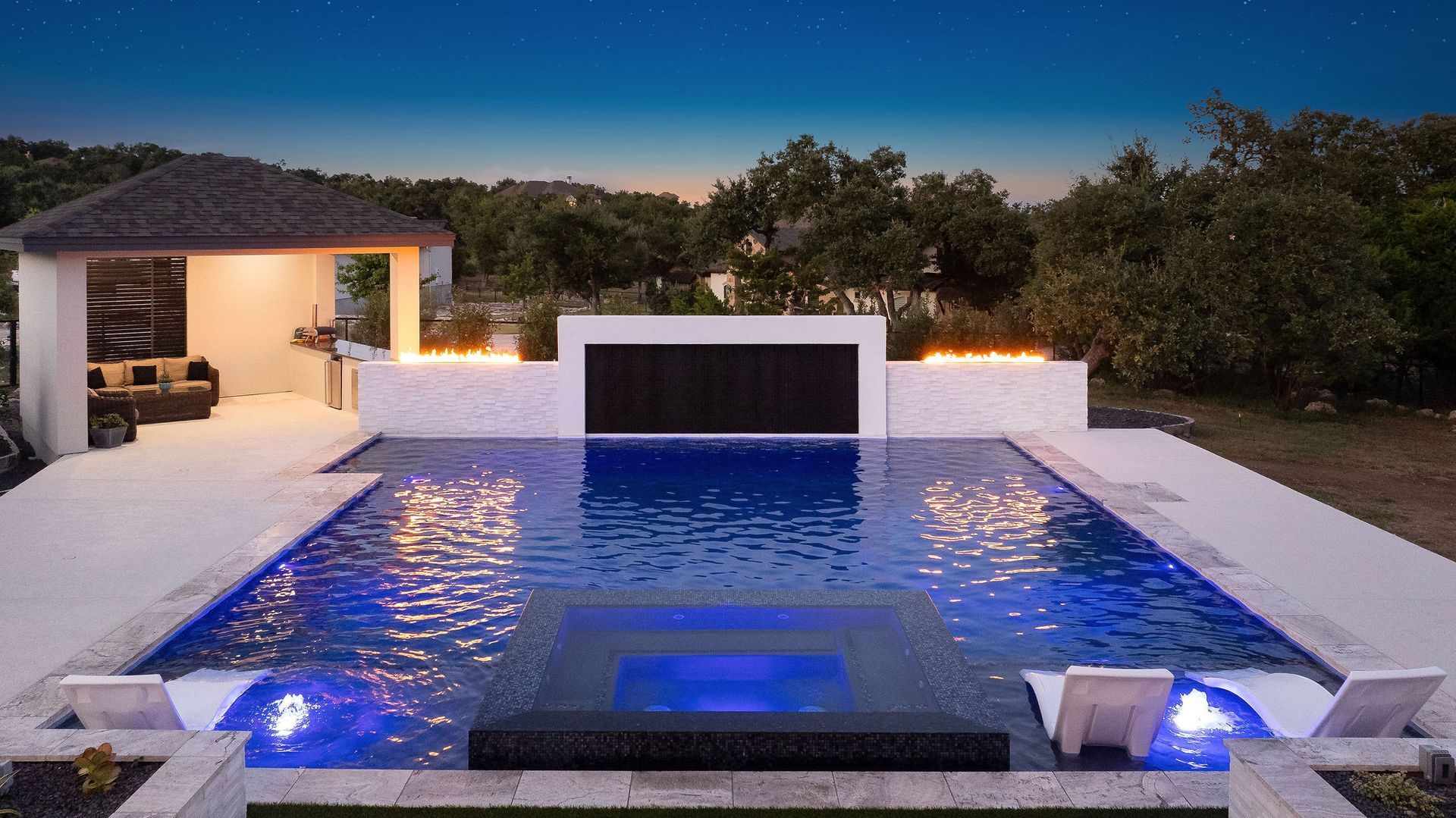 Luxury villa courtyard with lit swimming pool at sunset and surrounding white buildings