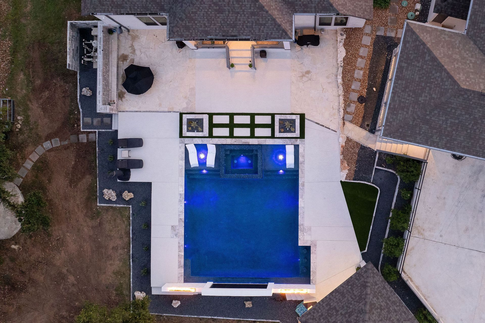 Luxury villa courtyard with lit swimming pool at sunset and surrounding white buildings