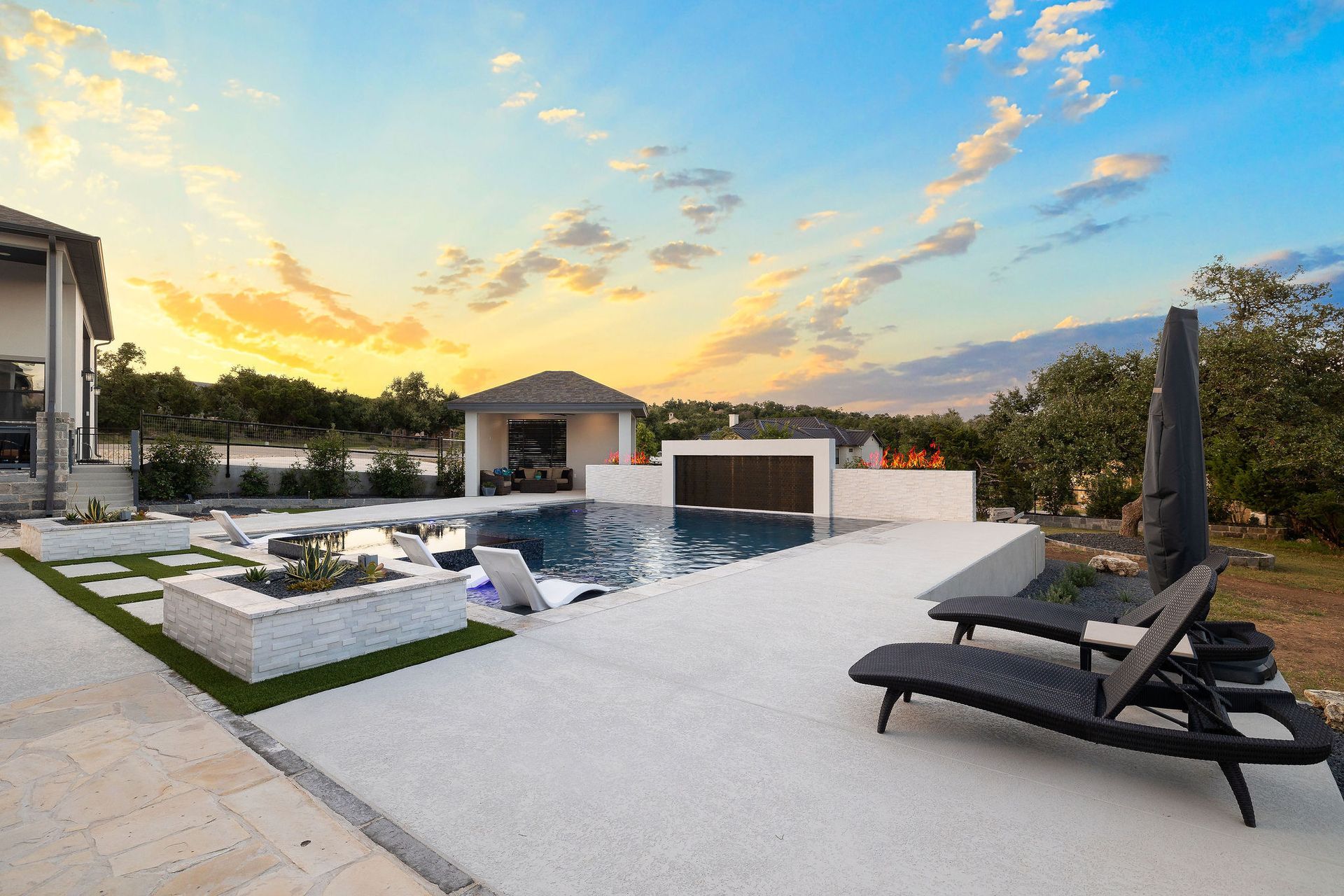 Modern backyard with a pool, white patio, lounge chairs, and a sunset sky
