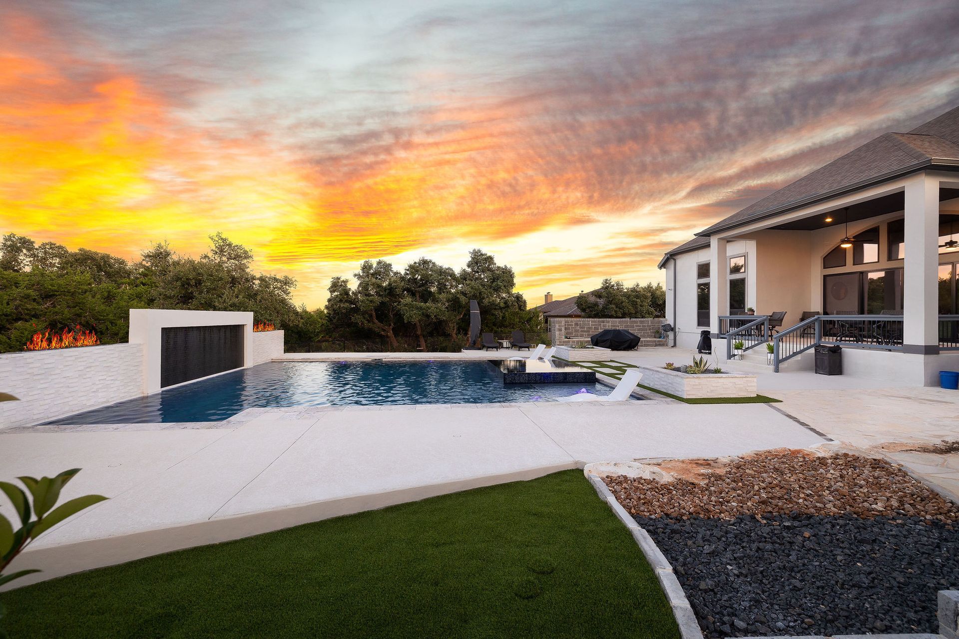Modern backyard with a pool, white patio, lounge chairs, and a dramatic sunset sky