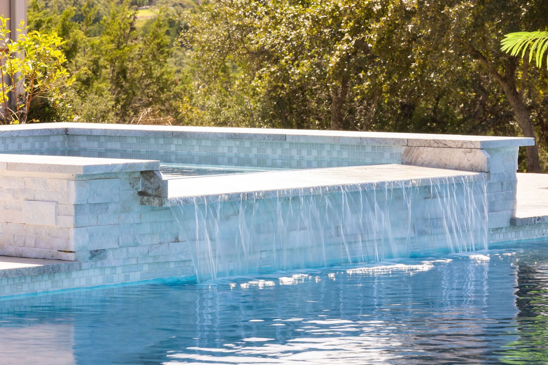 Luxury home with a covered patio beside a blue backyard swimming pool under a sunny sky