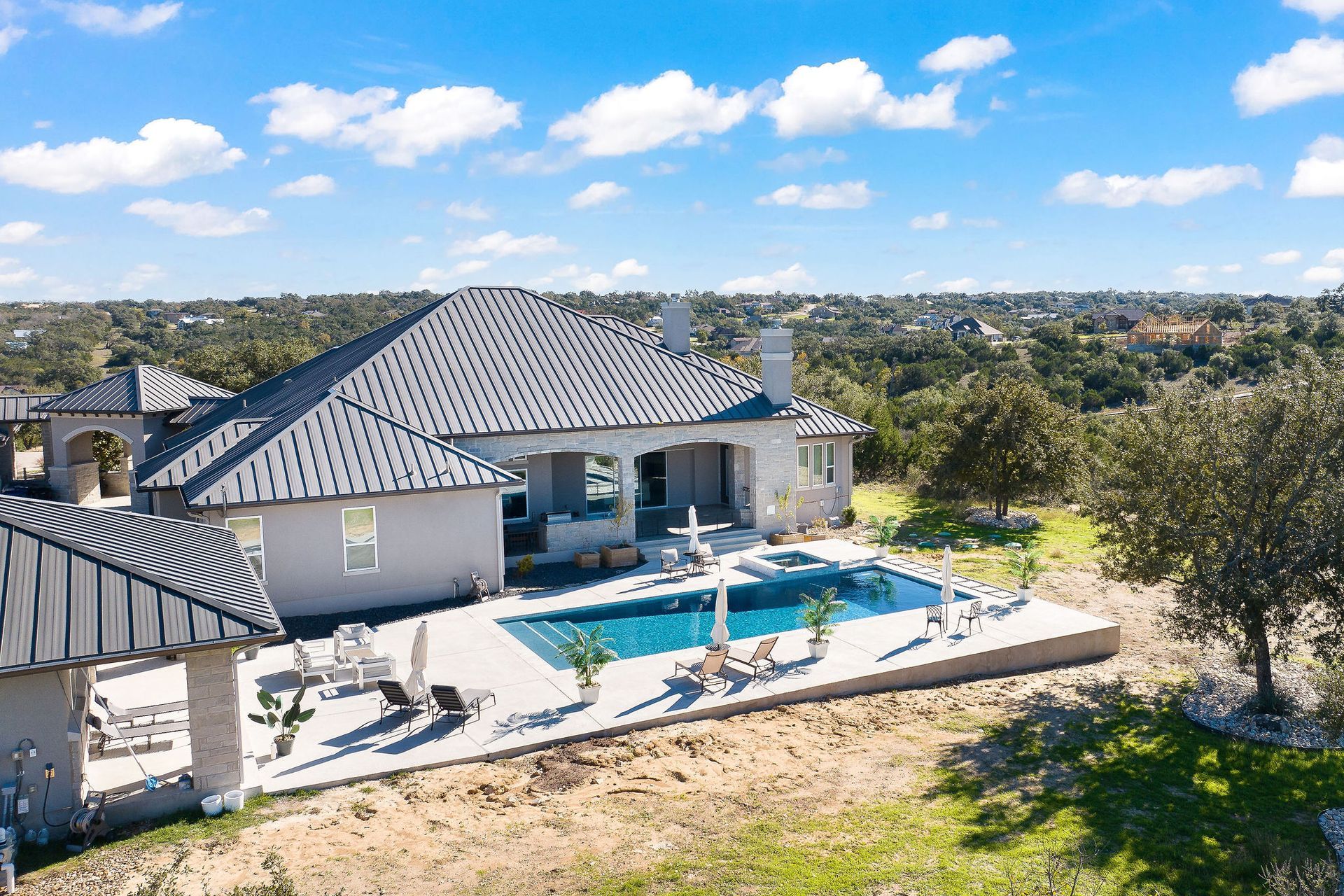 Luxury home with a covered patio beside a blue backyard swimming pool under a sunny sky