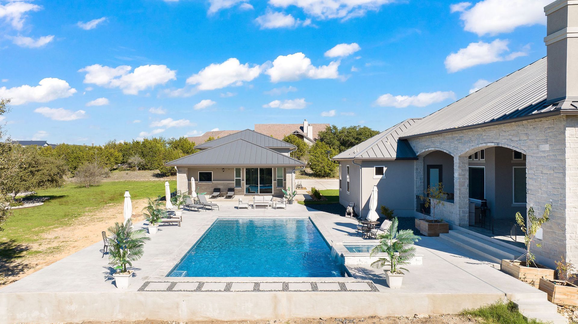 Luxury home with a covered patio beside a blue backyard swimming pool under a sunny sky