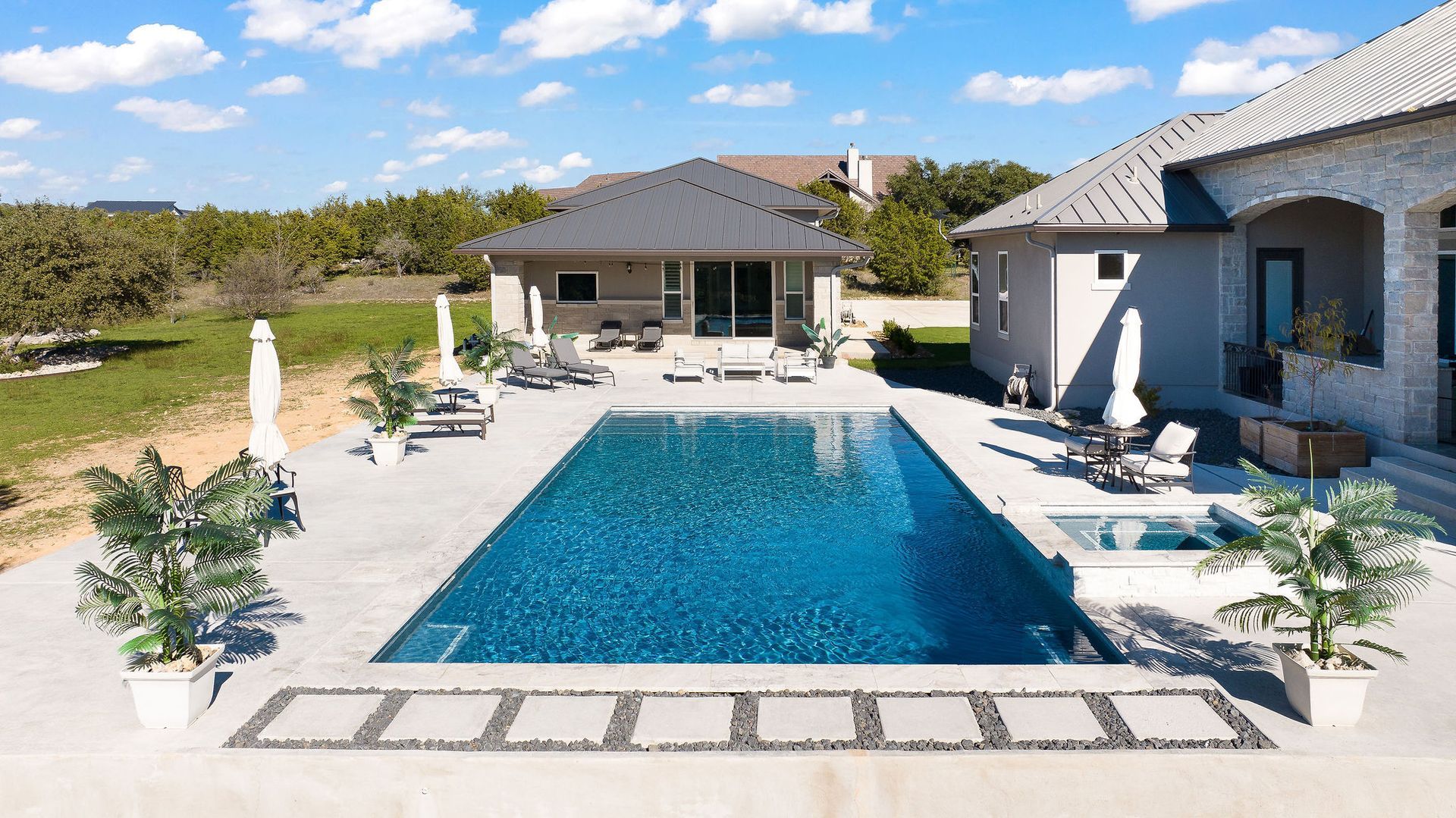 Luxury home with a covered patio beside a blue backyard swimming pool under a sunny sky