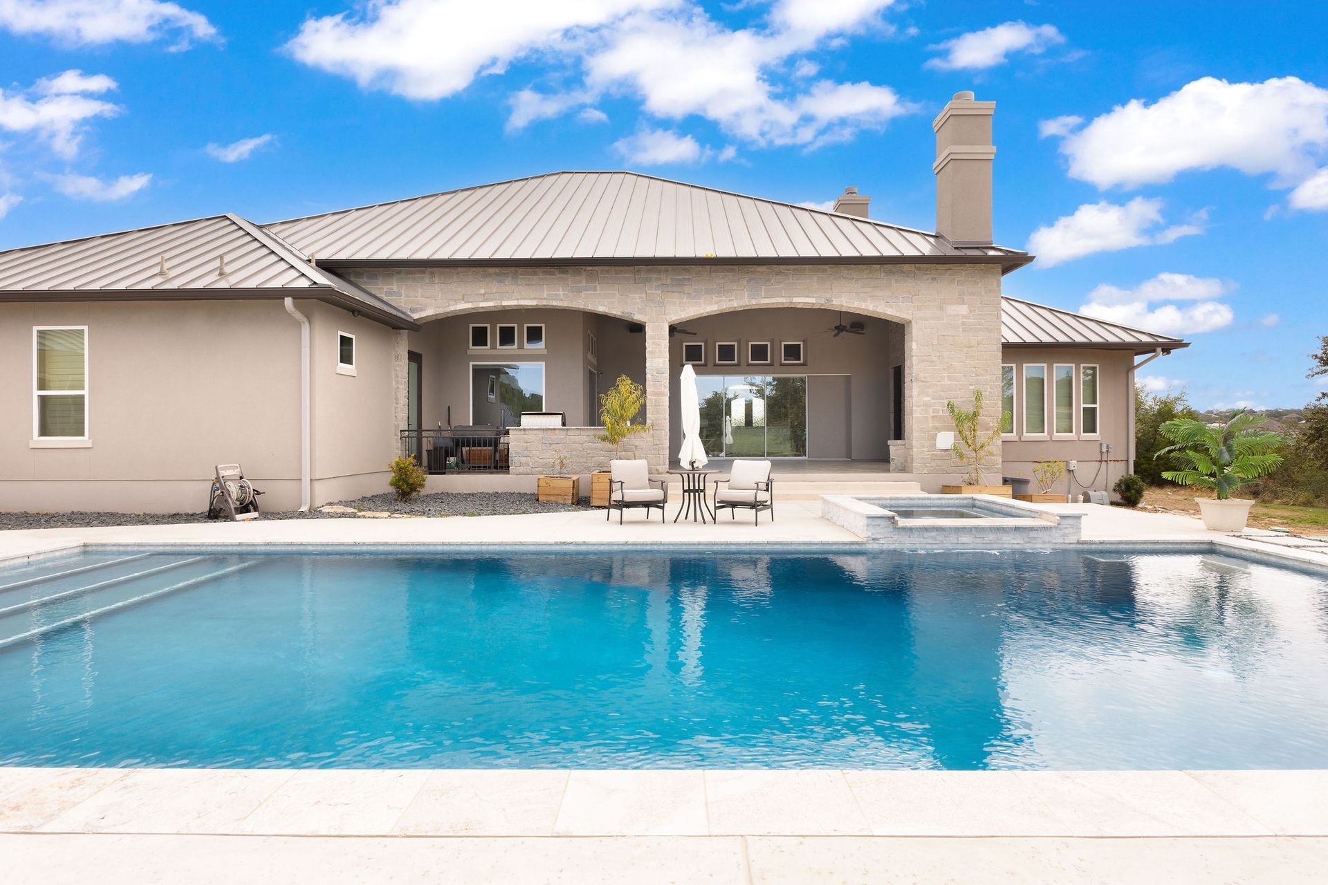Luxury home with a covered patio beside a blue backyard swimming pool under a sunny sky