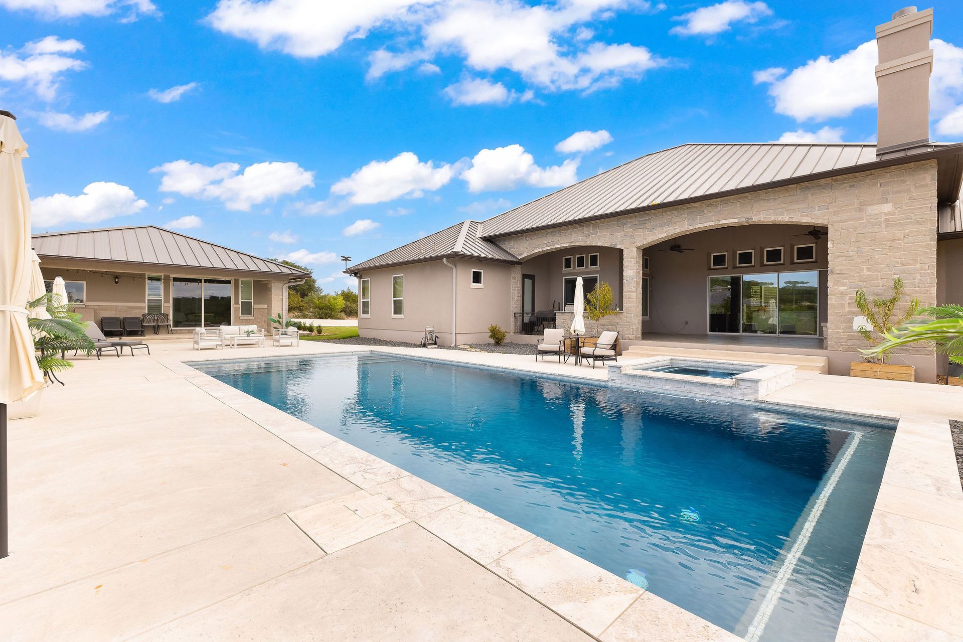 Luxury home with a covered patio beside a blue backyard swimming pool under a sunny sky