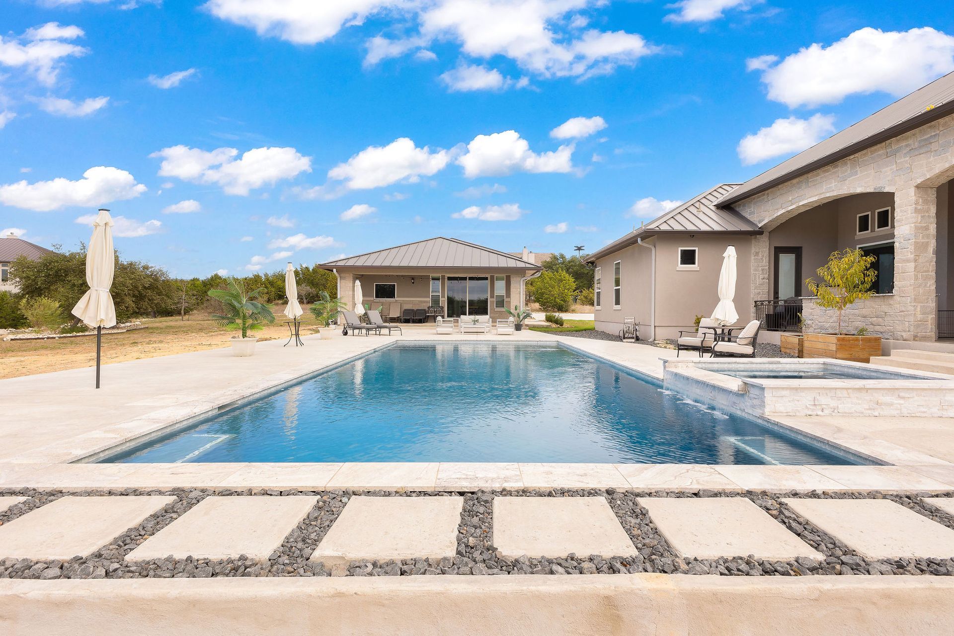Luxury home with a covered patio beside a blue backyard swimming pool under a sunny sky