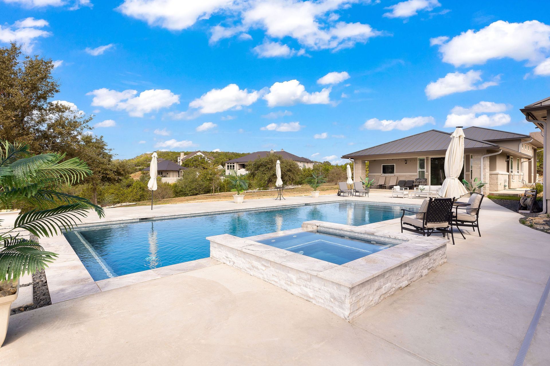 Luxury home with a covered patio beside a blue backyard swimming pool under a sunny sky