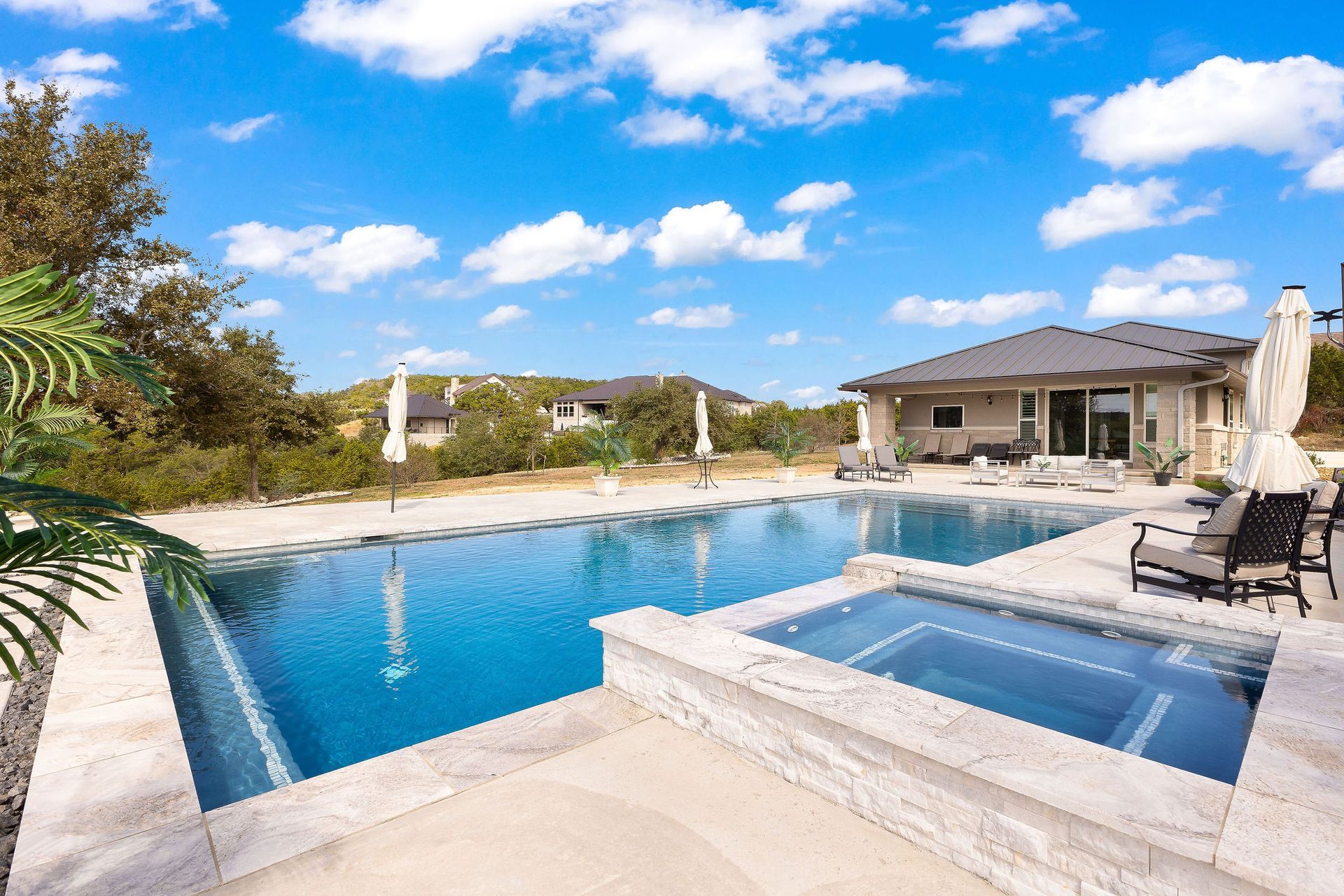 Luxury home with a covered patio beside a blue backyard swimming pool under a sunny sky