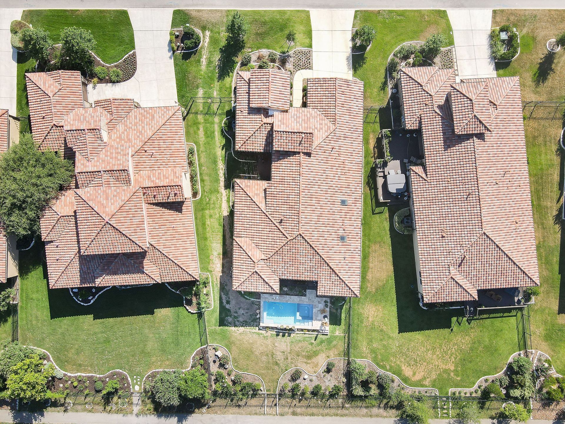 Aerial view of three houses with brown roofs and green lawns along a residential street.