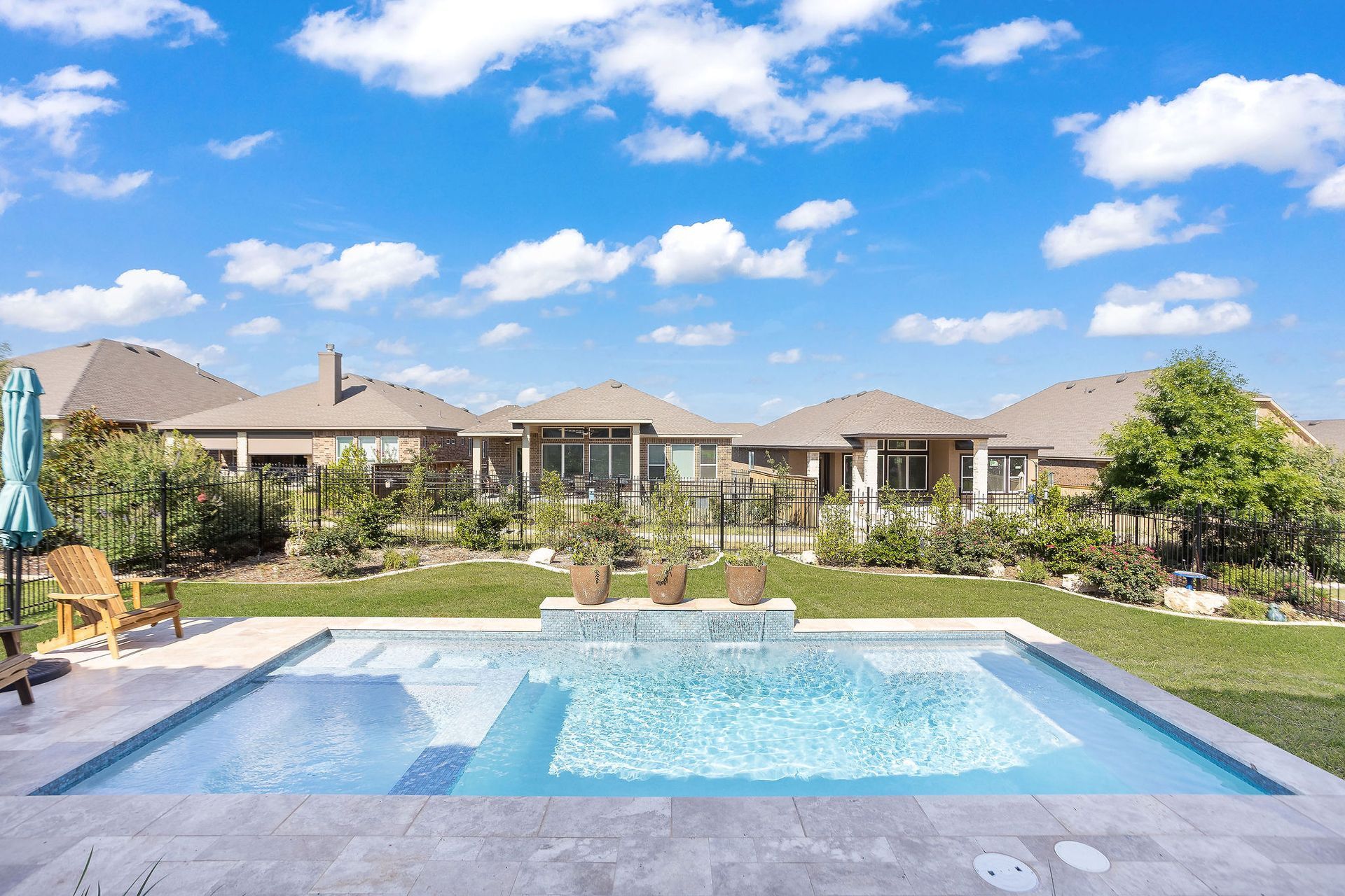 Backyard swimming pool in front of a row of tan houses under a blue sky with clouds