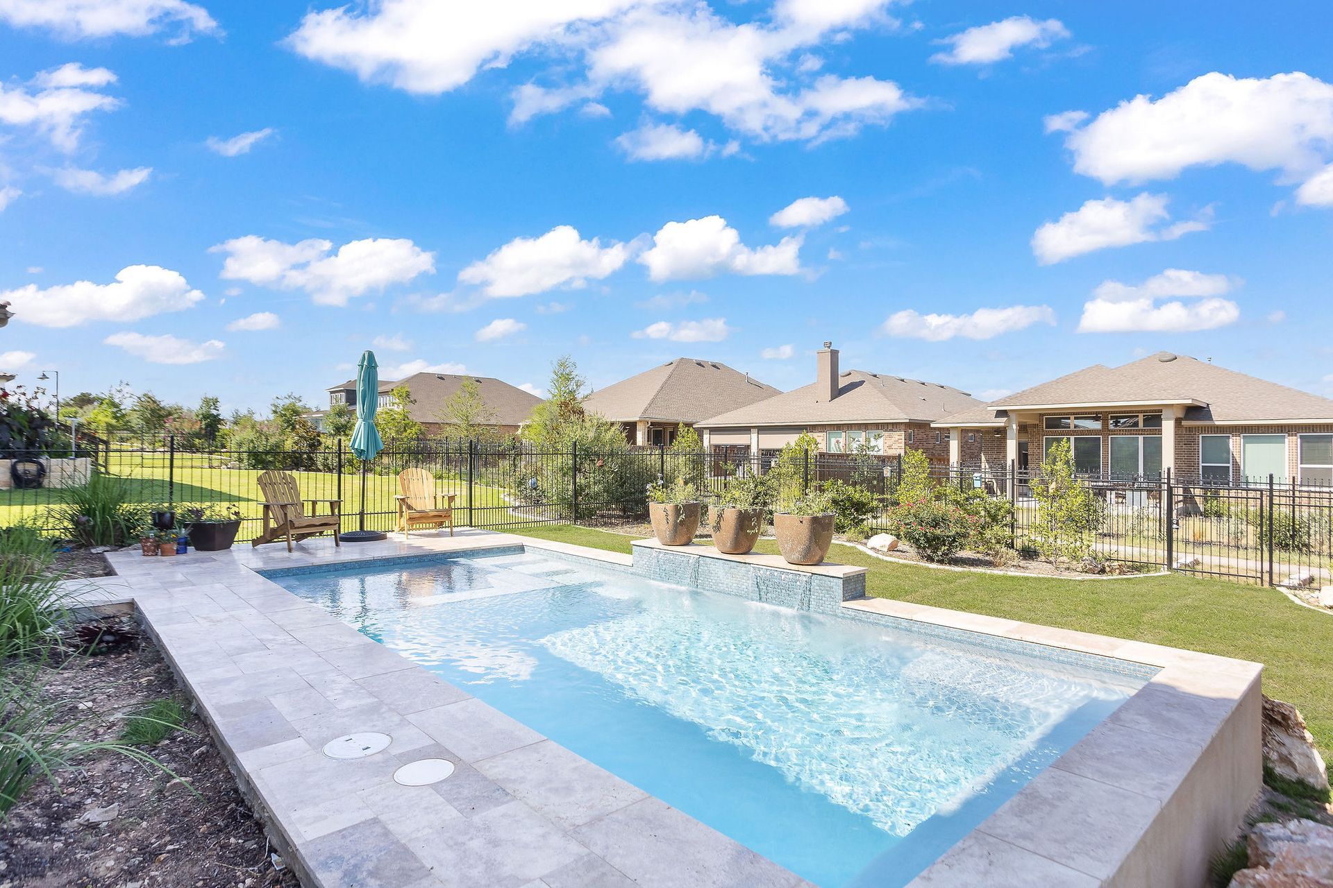 Backyard pool with lounge area and single-story homes under a bright blue sky