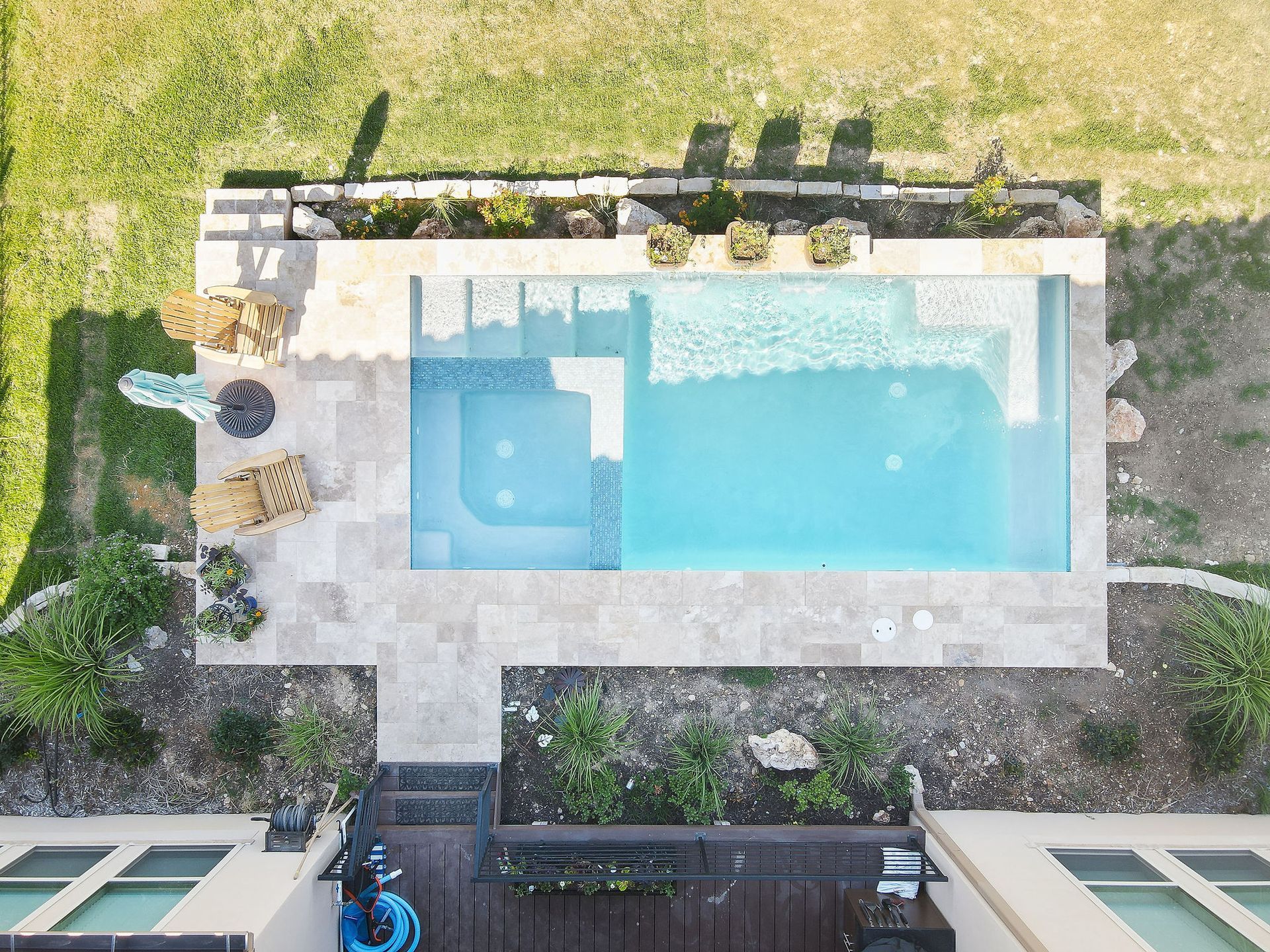 Top-down view of a backyard pool with blue water, stone deck, and lounge chairs amid greenery