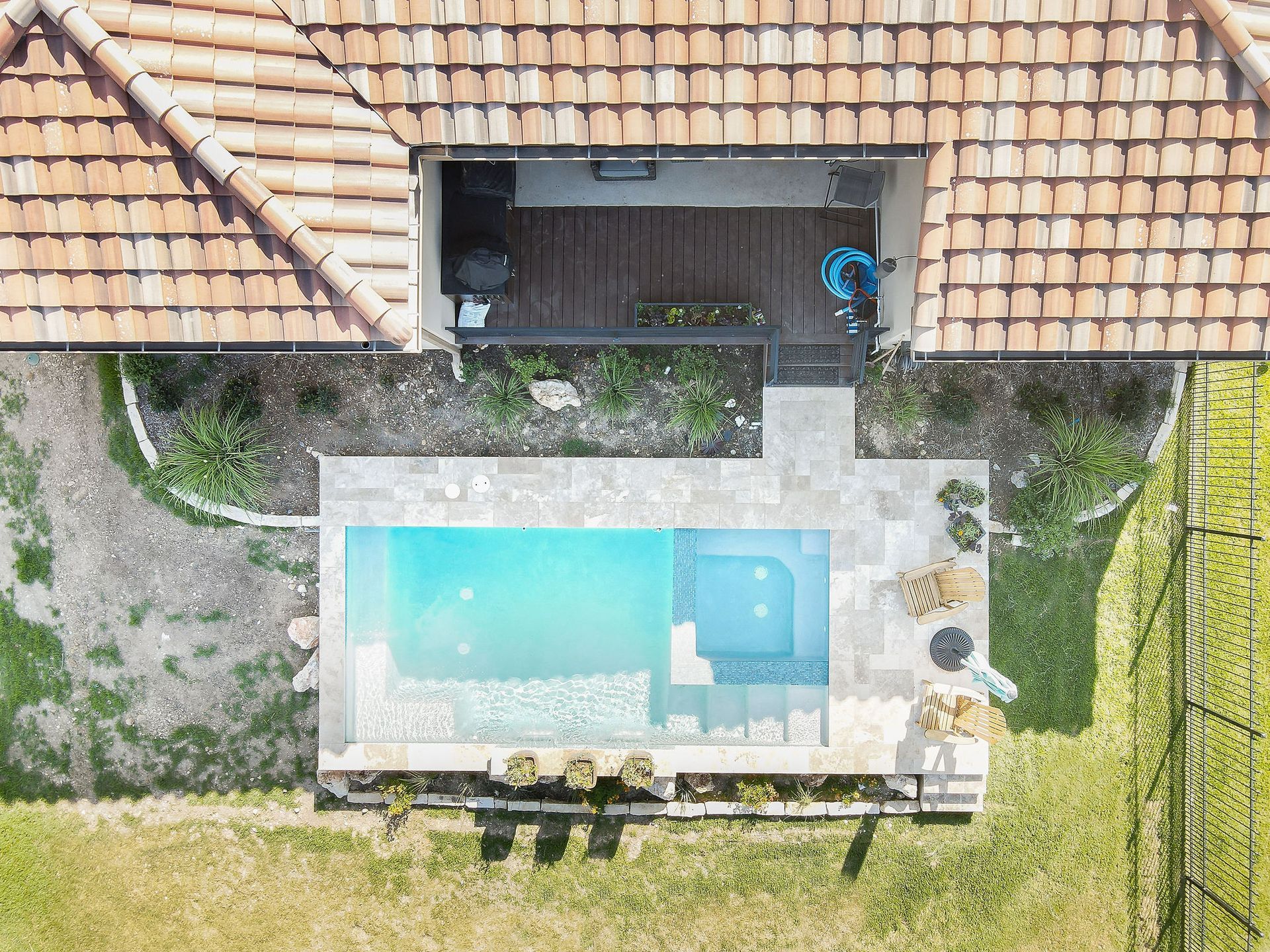 Aerial view of a backyard with a rectangular turquoise swimming pool beside a tiled roof