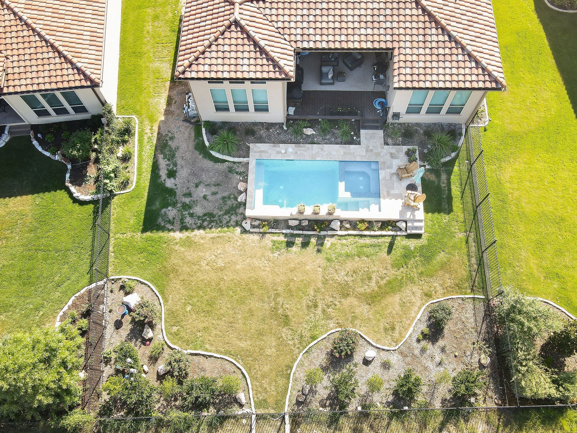Aerial view of a house with a backyard pool, patio, and lawn bordered by landscaped garden beds