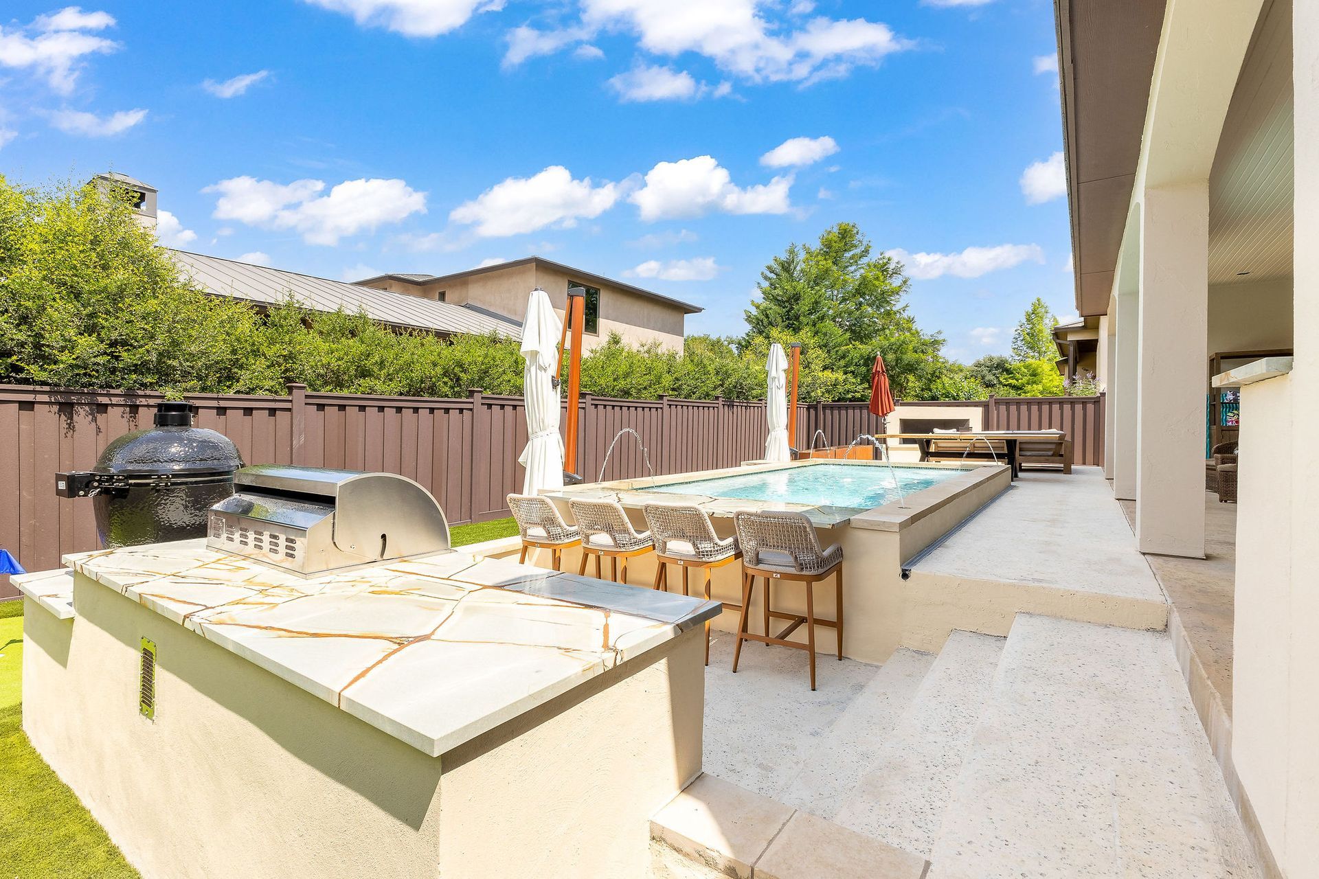Patio with outdoor dining table, grill, and lounge chairs beside a house under a blue sky
