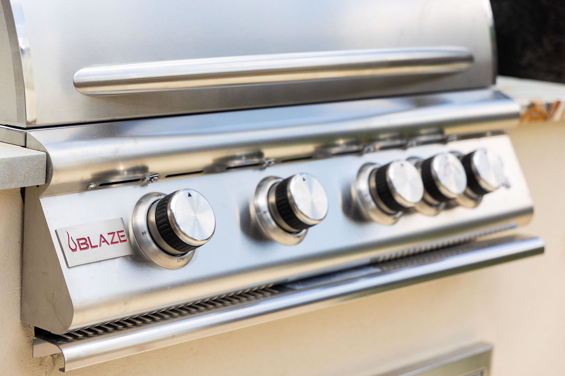 Close-up of a stainless steel gas grill with four control knobs and a side handle