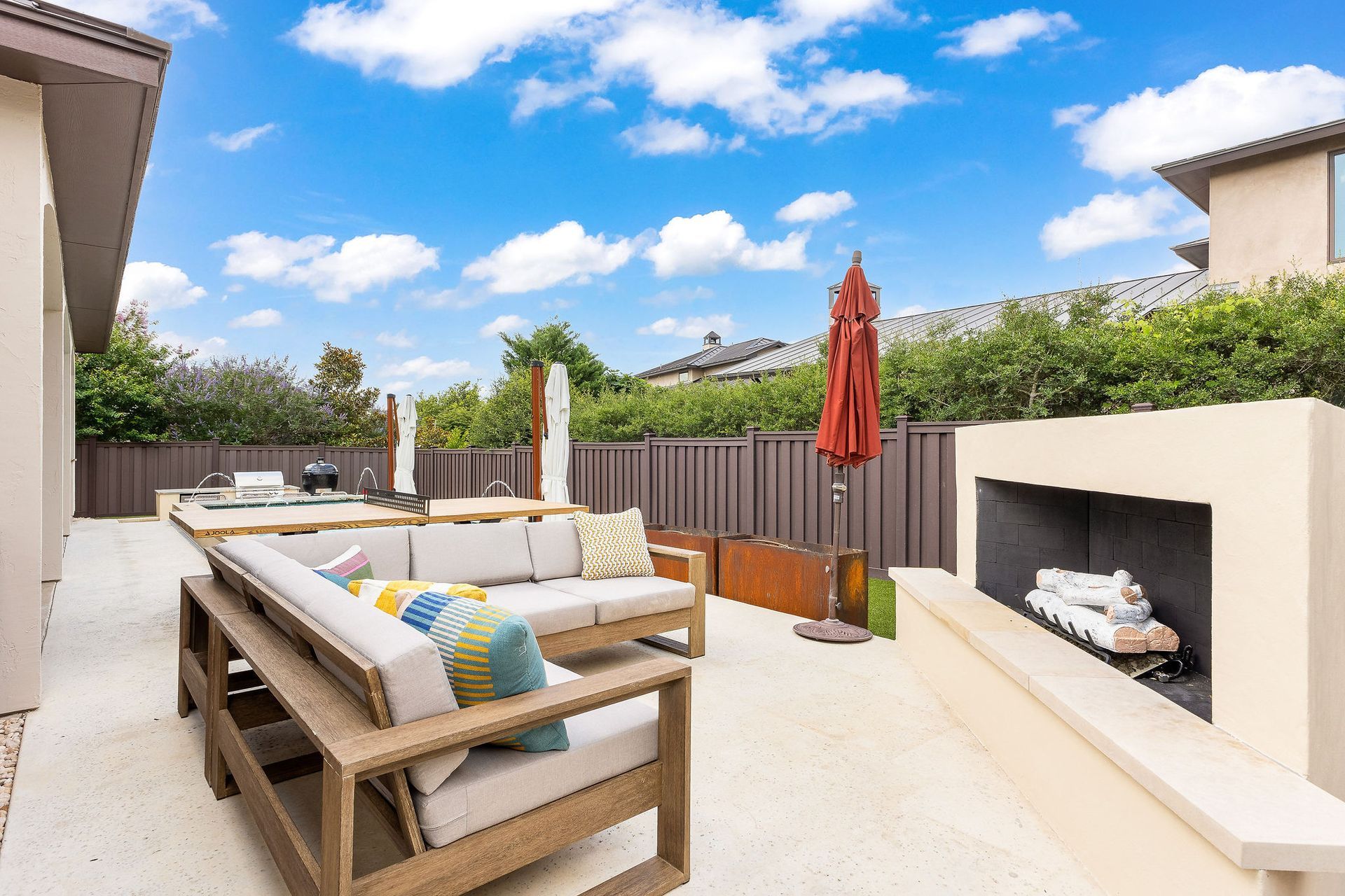 Modern patio with sectional sofa, fireplace, red umbrella, and blue sky with clouds