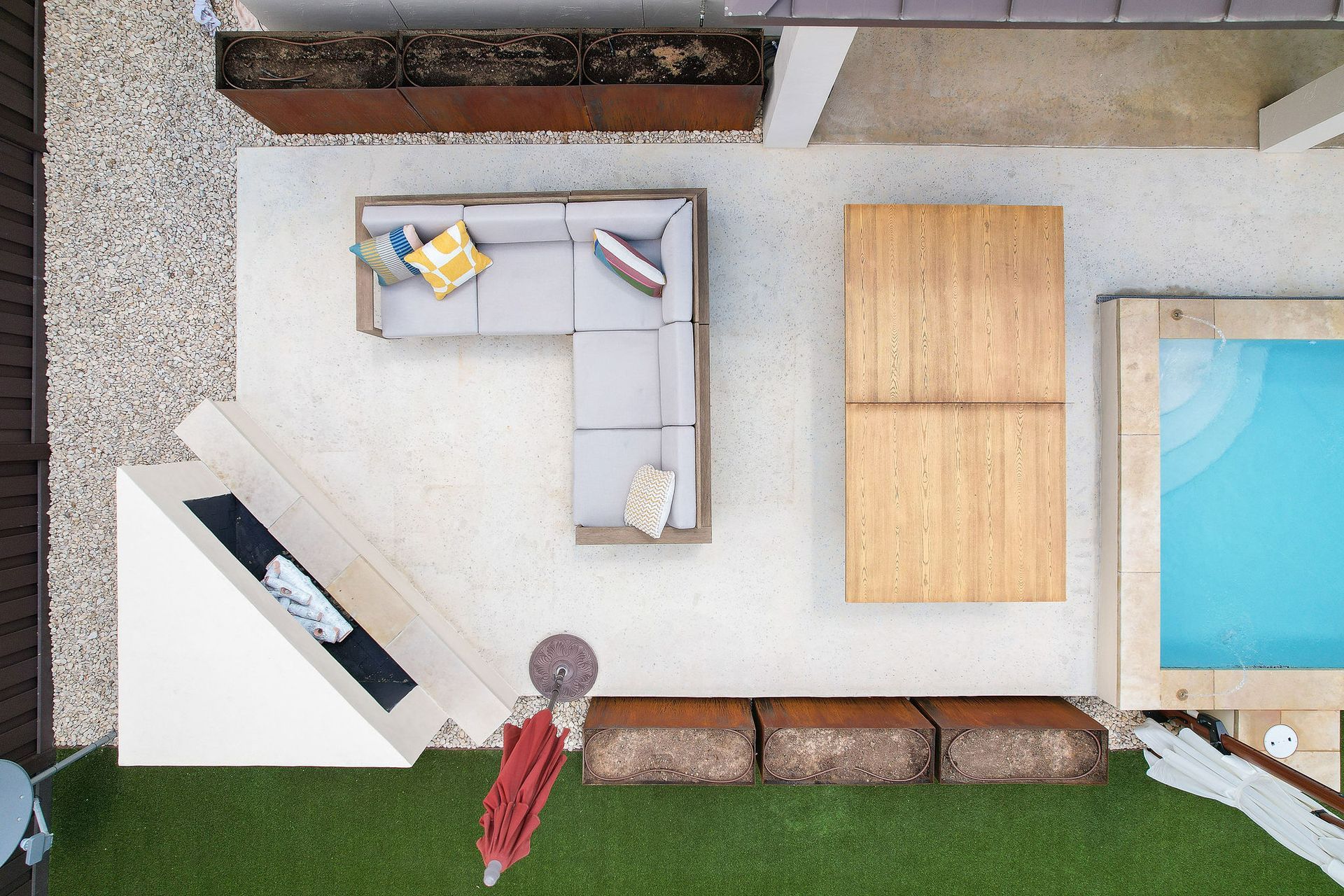 Overhead view of a modern patio with L-shaped sofa, lounge chair, table, lawn, and a pool edge