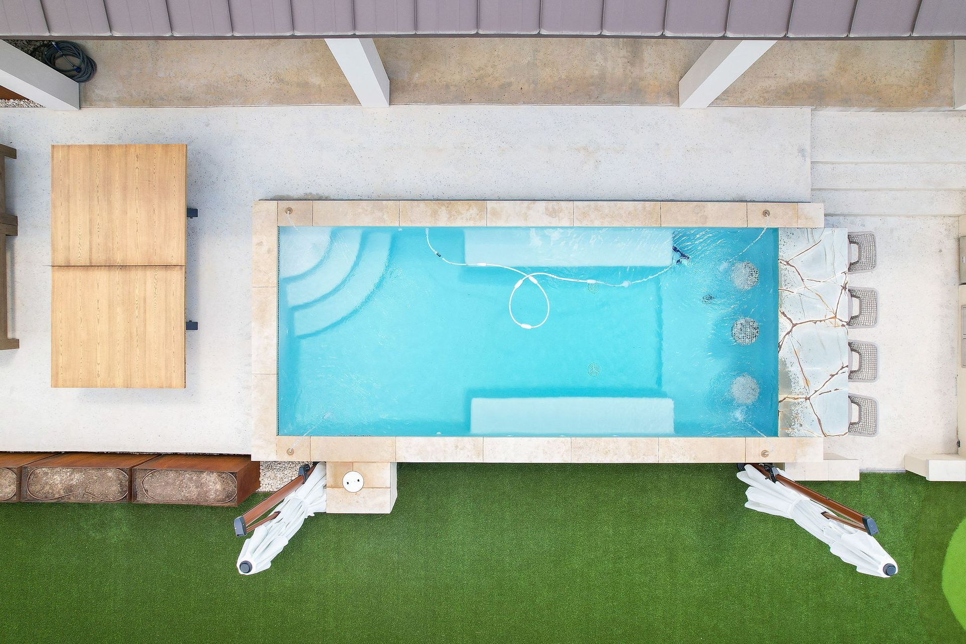 Overhead view of a turquoise backyard pool with loungers, chairs, and green lawn nearby