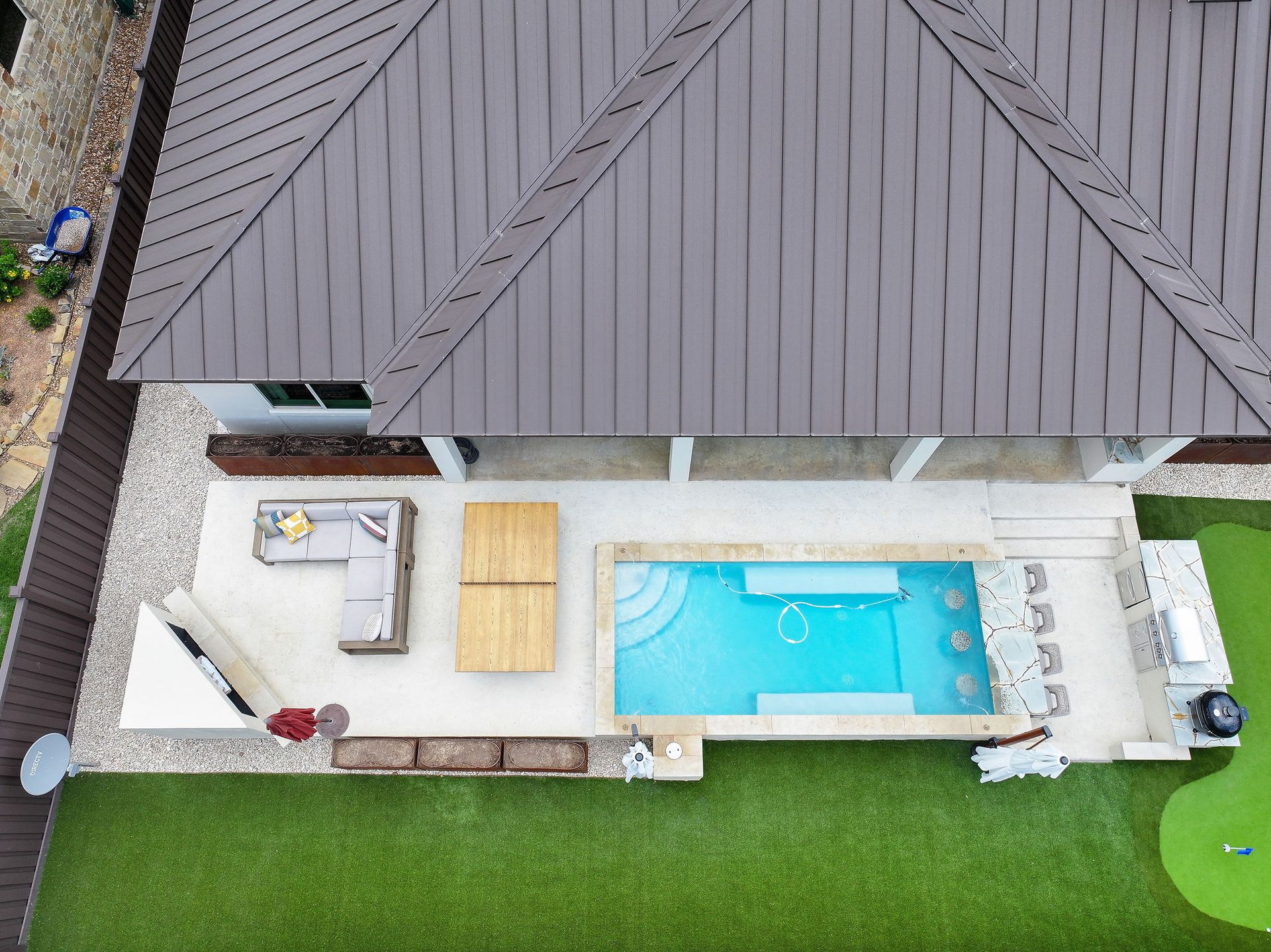 Aerial view of a modern home patio with a small pool, lounge chairs, and bright green lawn.