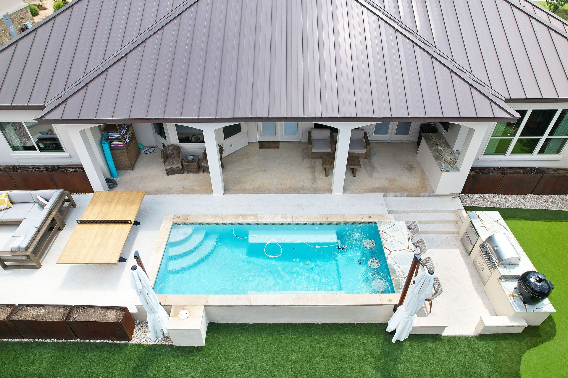 Aerial view of a backyard with a small pool beside a covered patio and green lawn