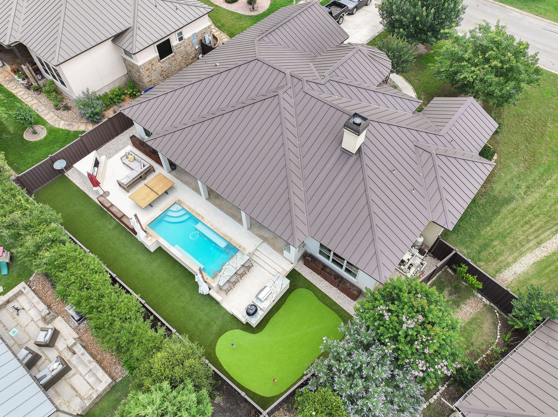 Aerial view of a house with a backyard pool, patio, and green lawn surrounded by a fence.