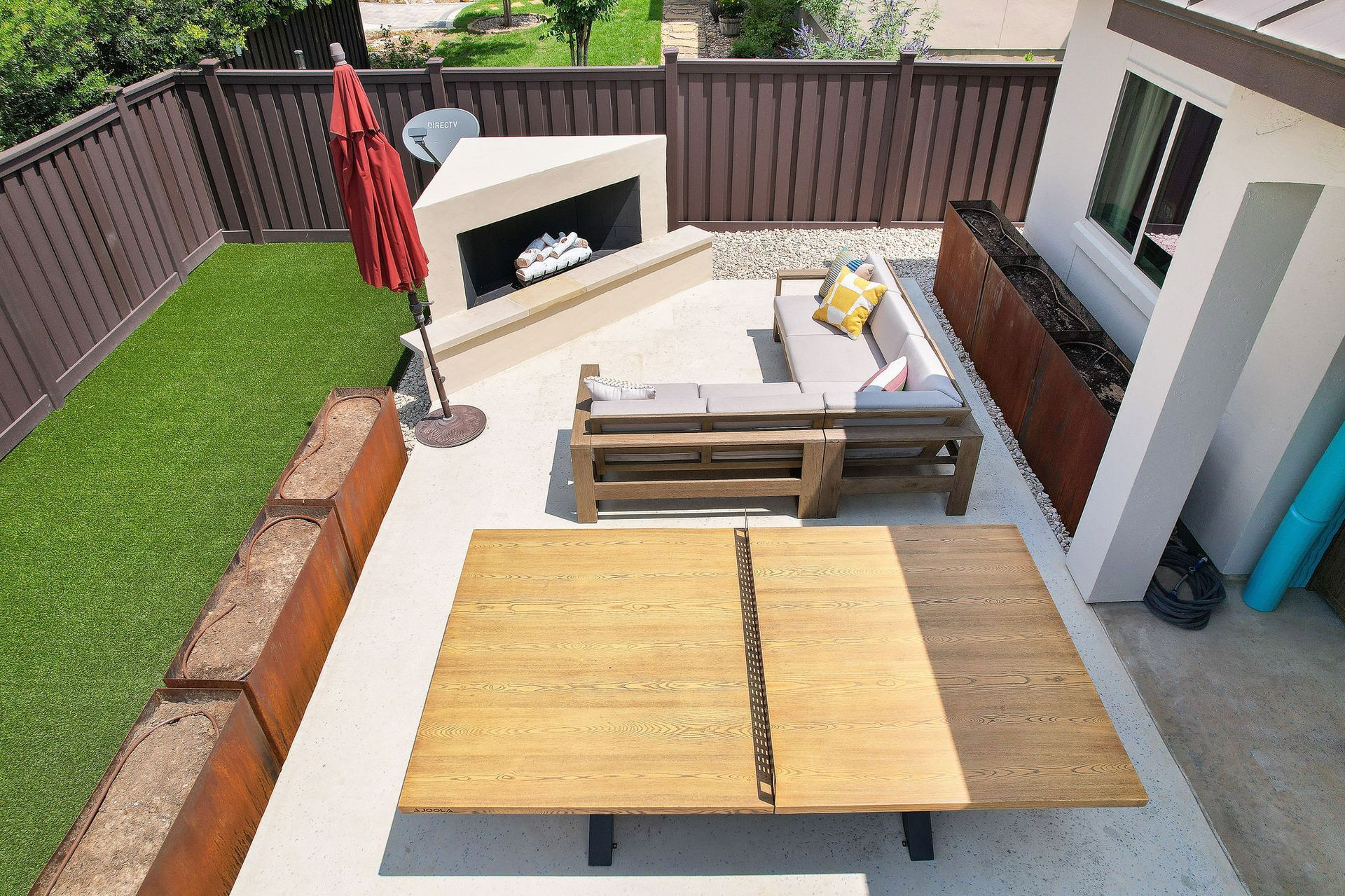 Backyard patio with fire pit, lounge chairs, and wooden picnic table on concrete decking