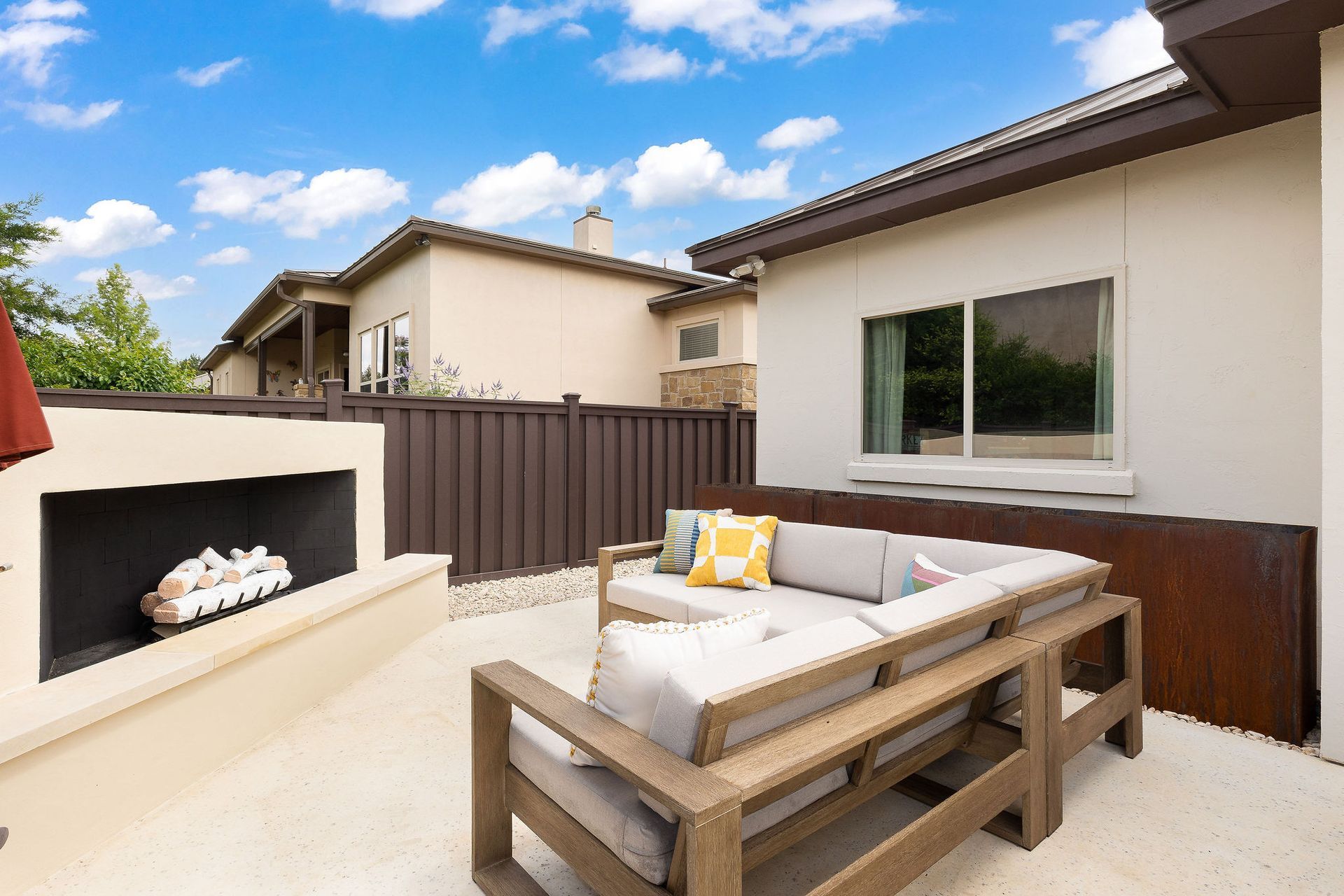 Patio with a cushioned wooden sofa, built-in grill, and fenced backyard under a blue sky