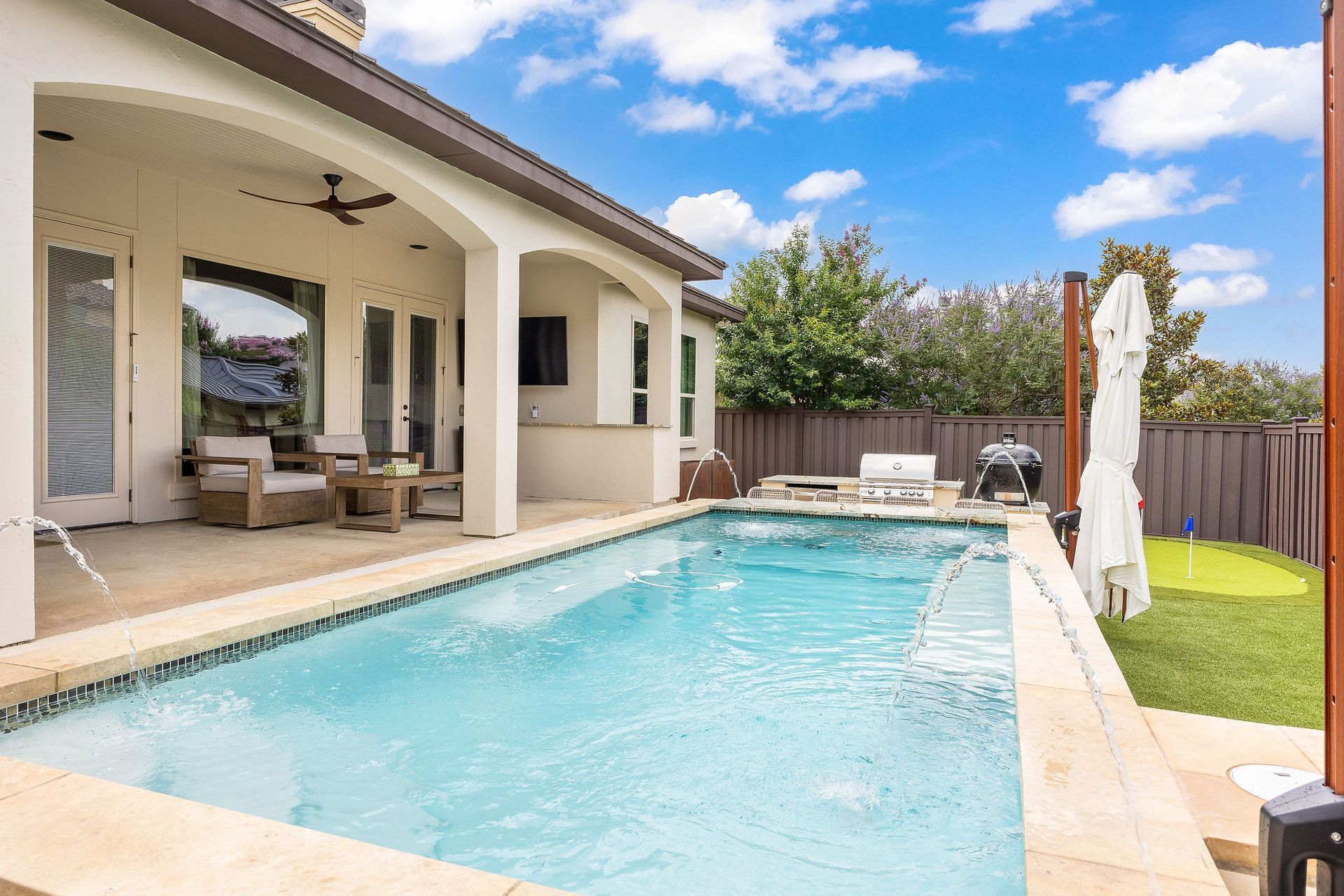Modern backyard with a swimming pool, covered patio, and lounge chairs on a sunny day
