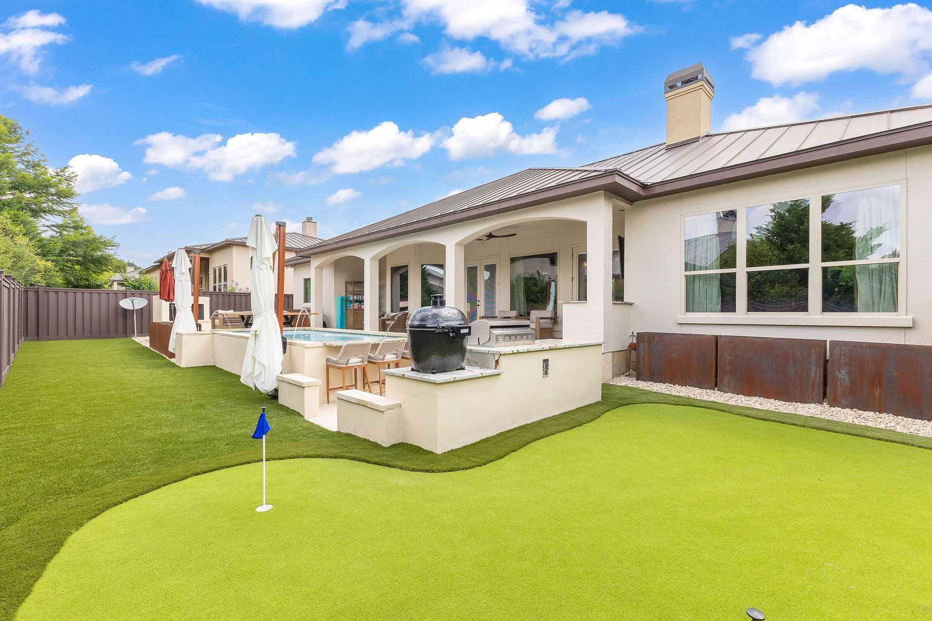 Backyard patio with green lawn, white stucco house, and covered outdoor seating area under a blue sky