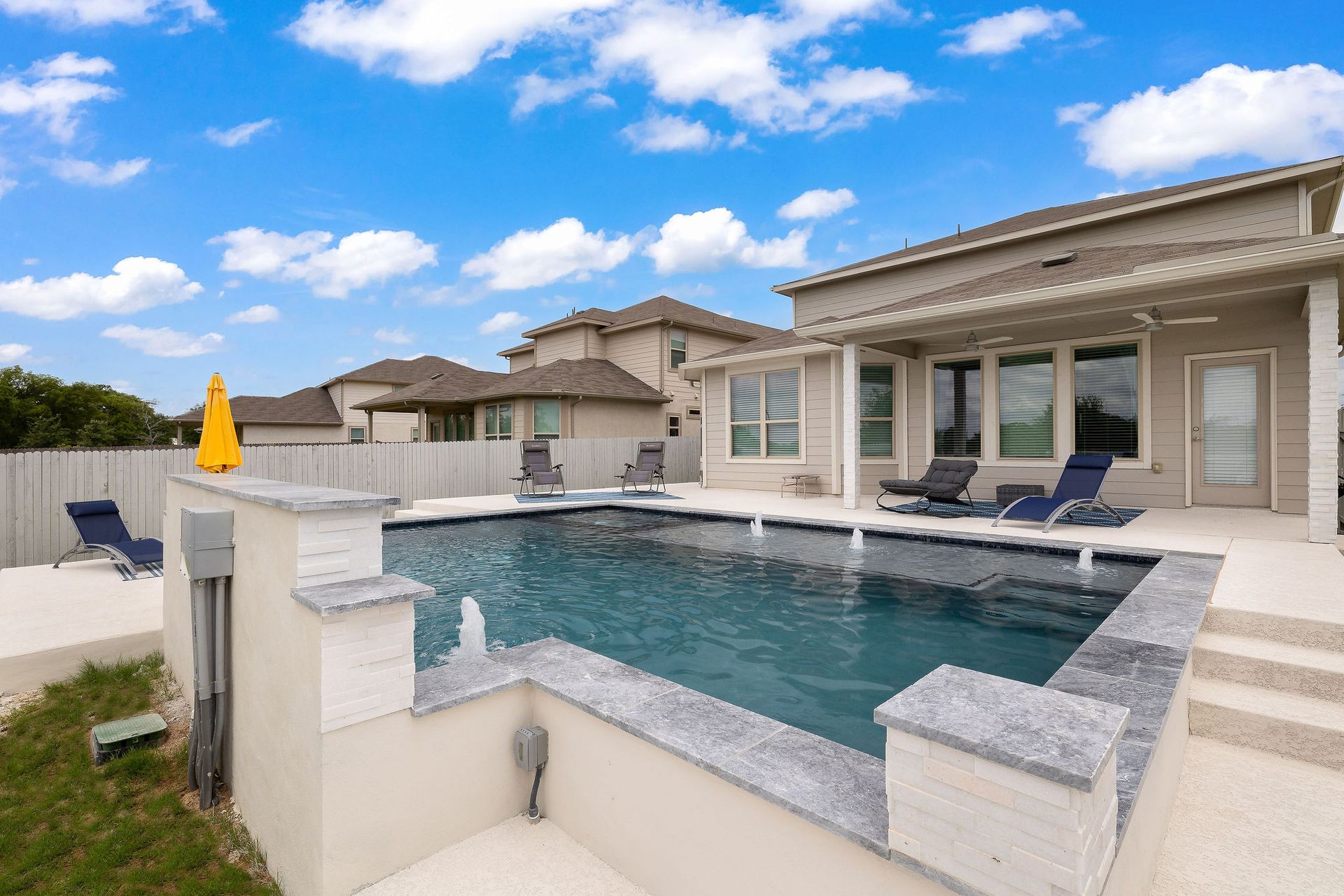 Backyard pool with patio, lounge chairs, and a modern house under a partly cloudy sky
