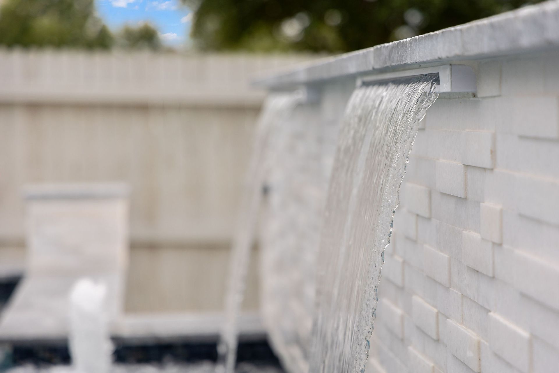 Water spilling from a white tiled pool wall into a backyard pool area.