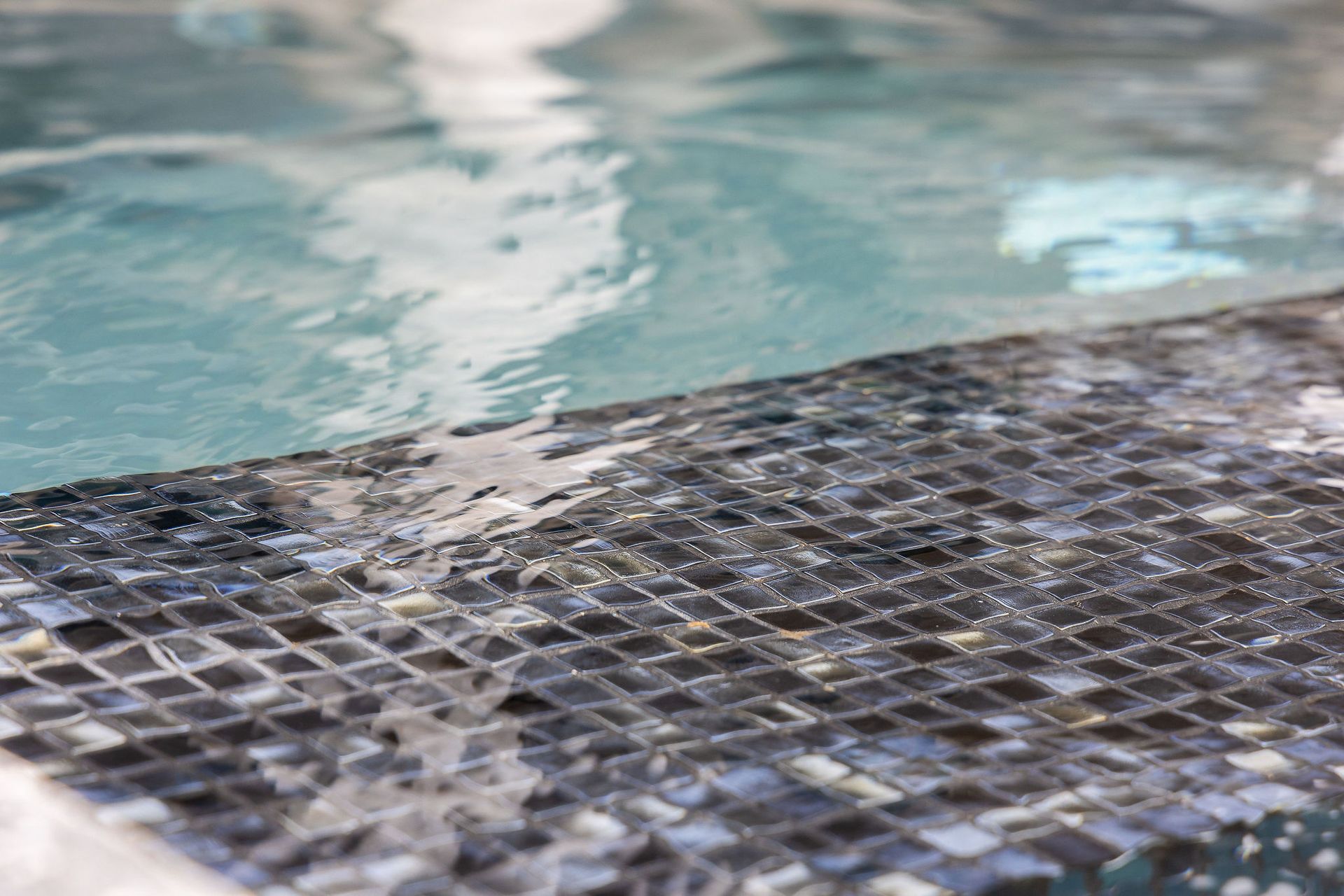 Mosaic tile pool edge beside rippling blue water