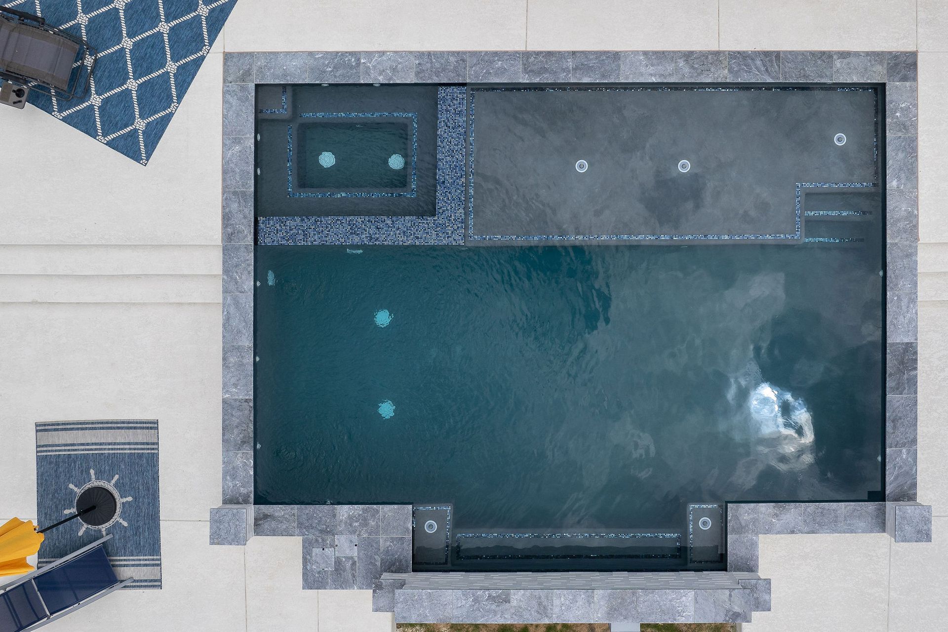 Overhead view of a backyard pool with gray stone decking and a small hot tub