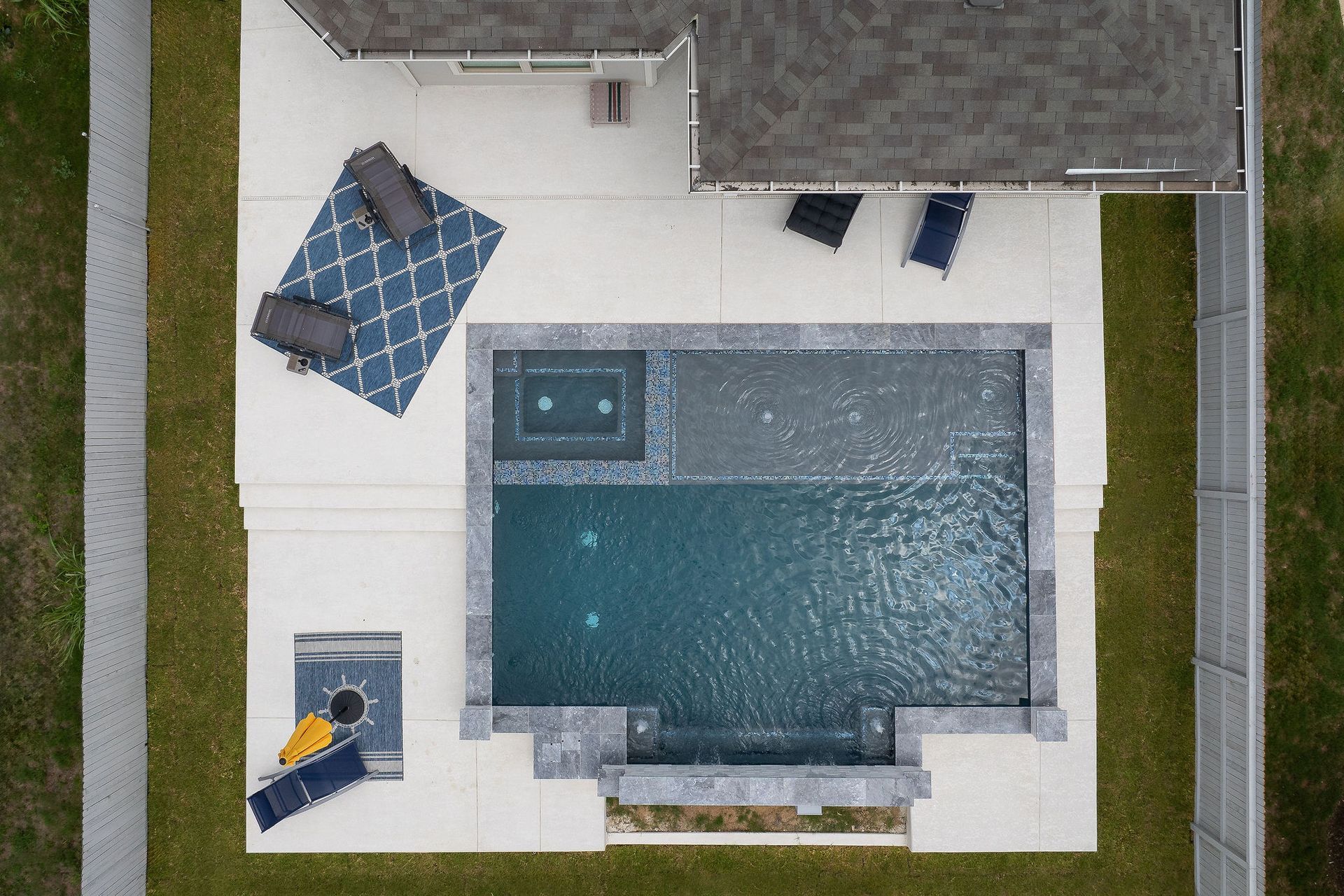 Overhead view of a backyard pool with lounge chairs, a patio table, and a small attached spa