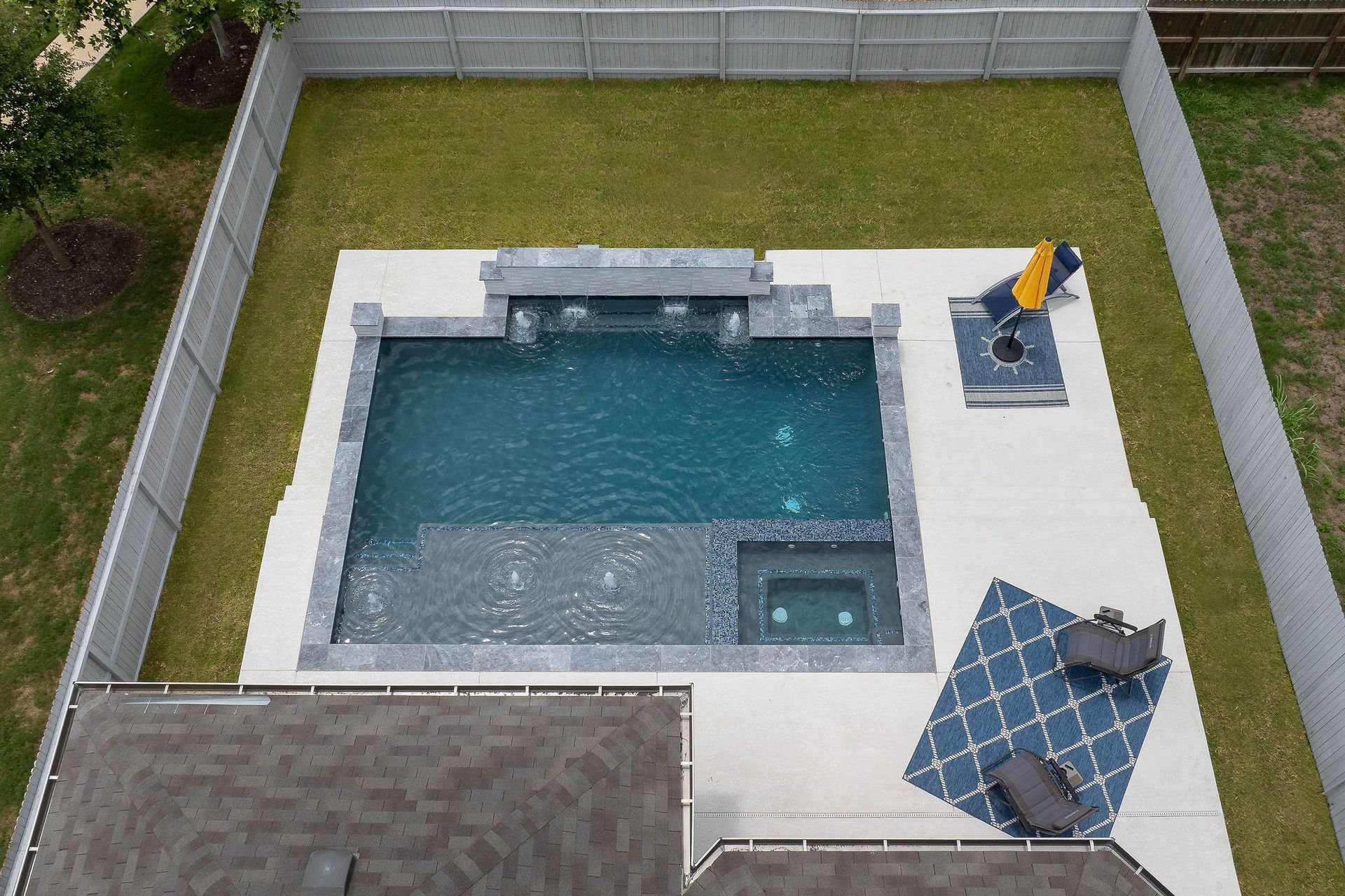 Backyard with a rectangular swimming pool, patio, umbrella table, and lounge chair enclosed by a fence