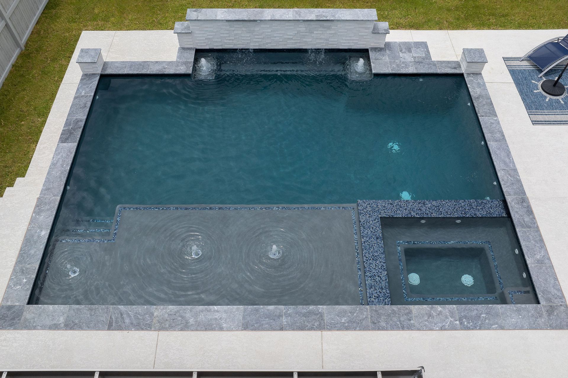 Modern backyard pool with gray stone decking and a small attached spa