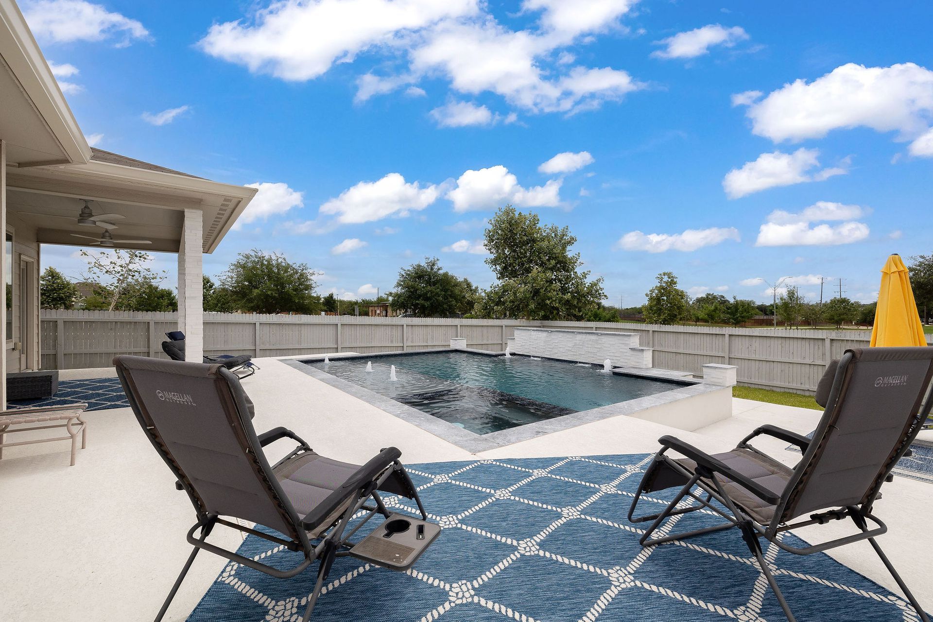 Patio with two lounge chairs facing a backyard swimming pool under a blue sky