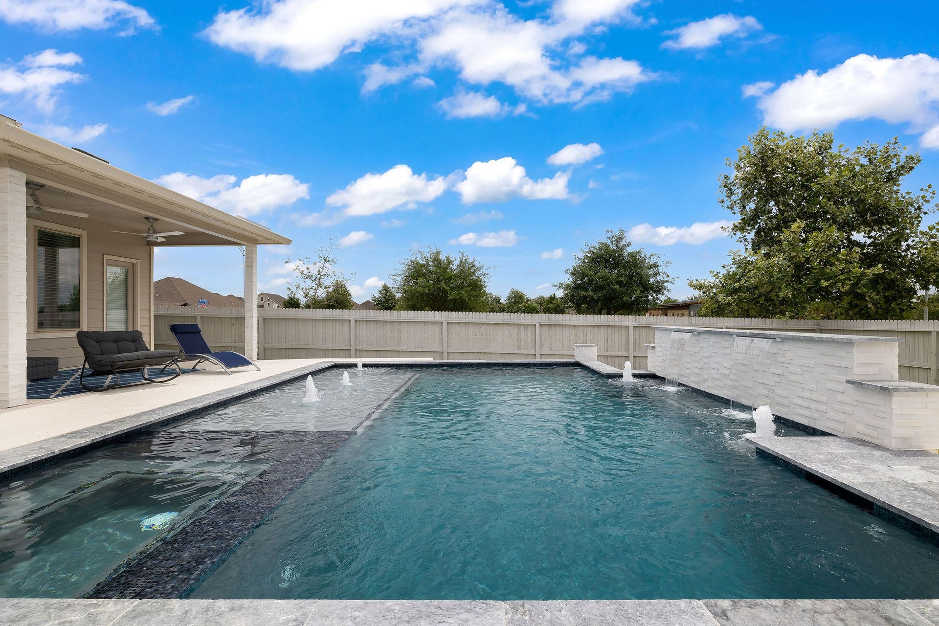 Backyard swimming pool with patio seating, stone walls, and a blue sky