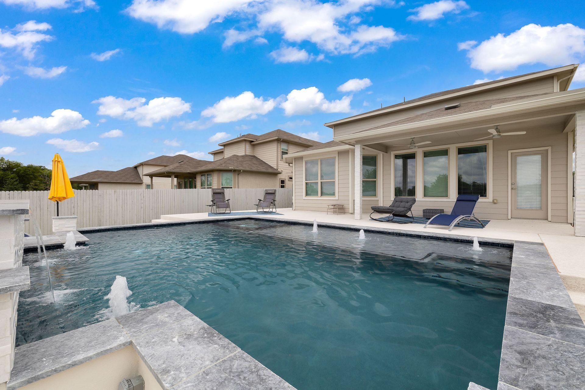 Modern backyard pool with spa, lounge chairs, and a patio under a bright blue sky